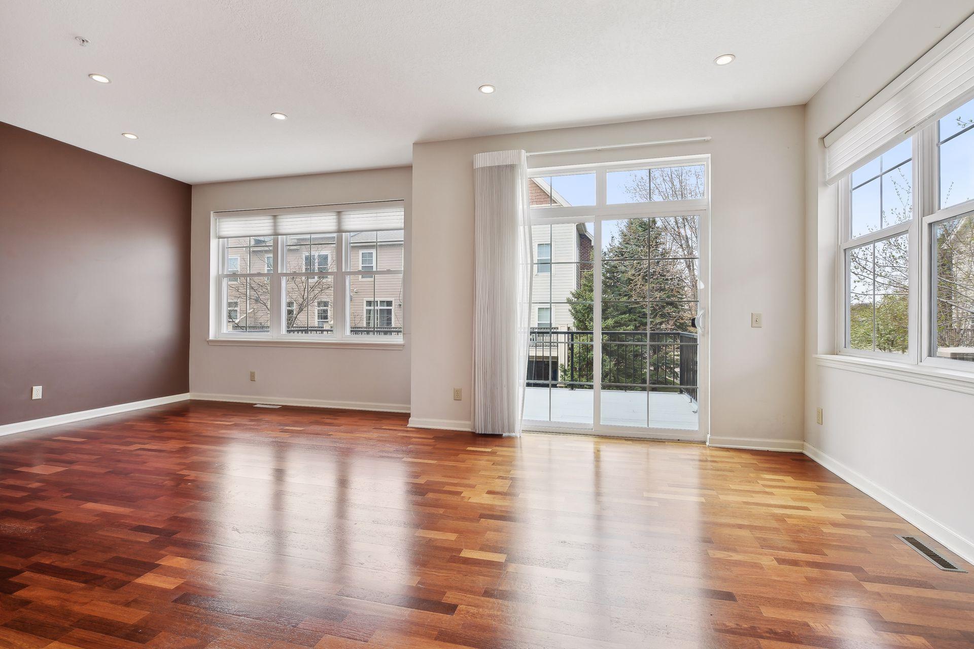 Unfurnished living room with hardwood floors, large windows, and a sliding glass door to the balcony.
