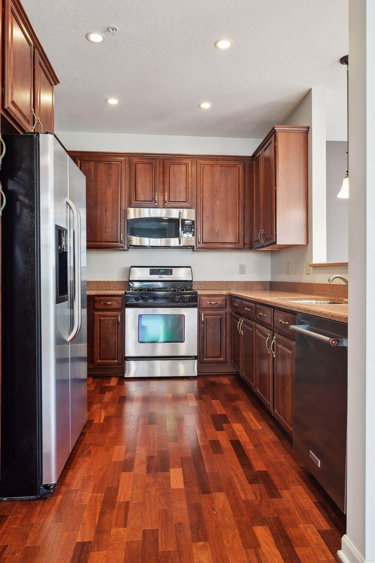 Kitchen with dark wood cabinets, granite counters, stainless steel appliances, and reddish hardwood floors.