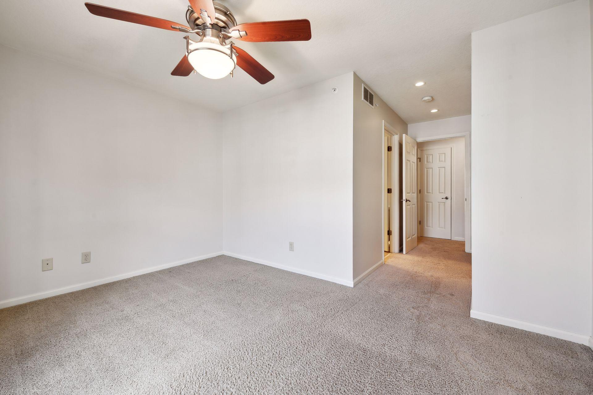 Empty carpeted bedroom with a wooden-blade ceiling fan and an open doorway to the hallway.