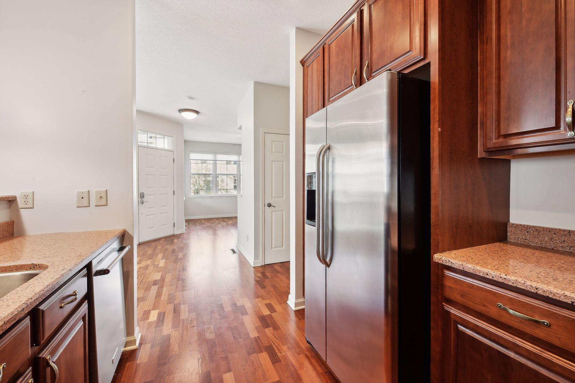 Kitchen with dark wood cabinets, speckled counters, and a stainless steel refrigerator beside the hardwood-floored entry.