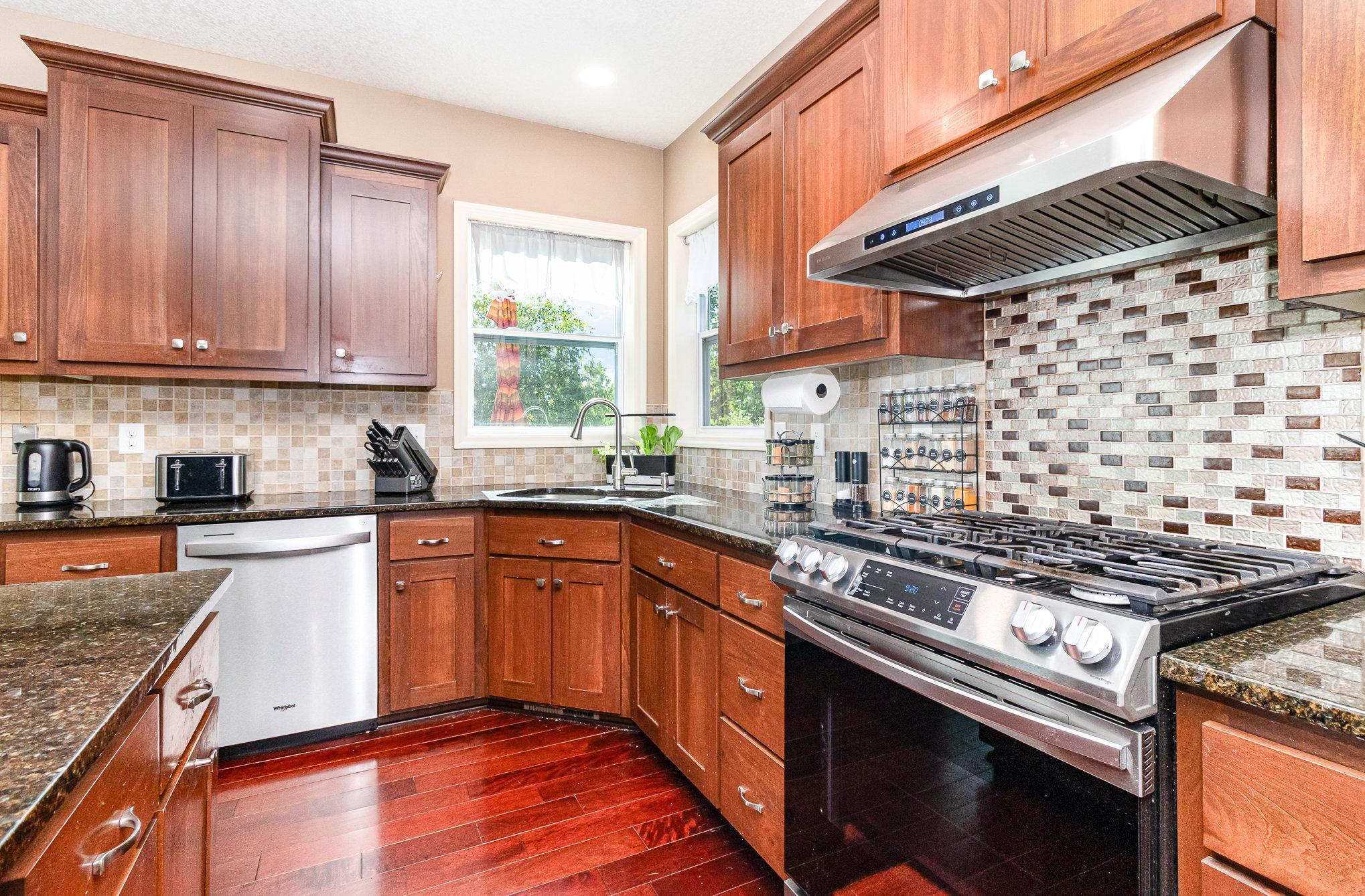 Kitchen with reddish wood cabinets, mosaic tile backsplash, and a prominent stainless steel gas range.