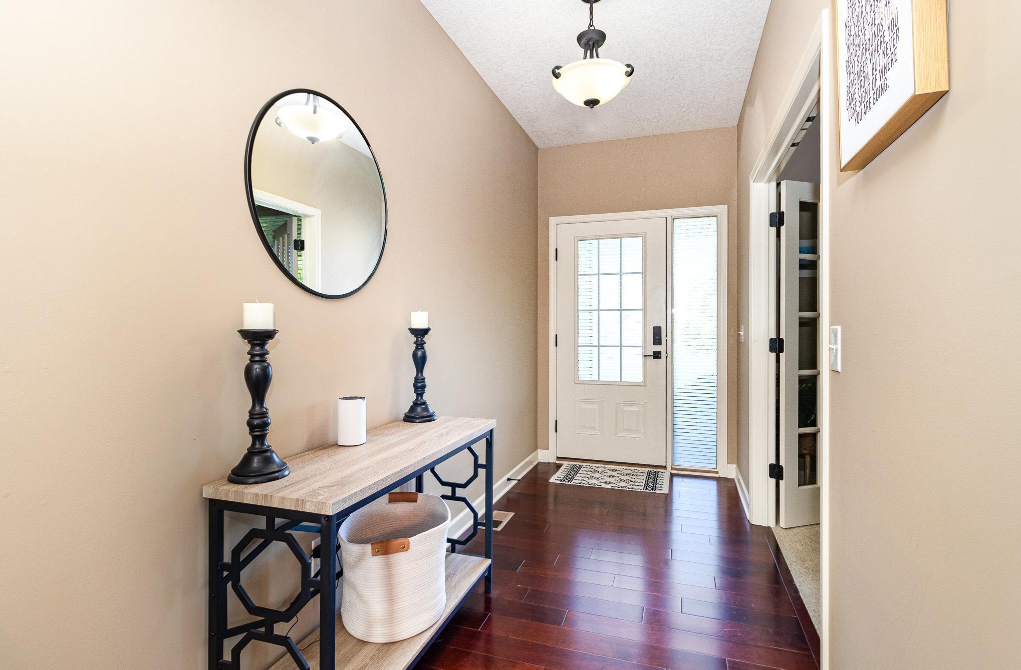 Furnished entryway with a glass-paneled front door, dark wood floors, and a console table beneath an oval mirror.