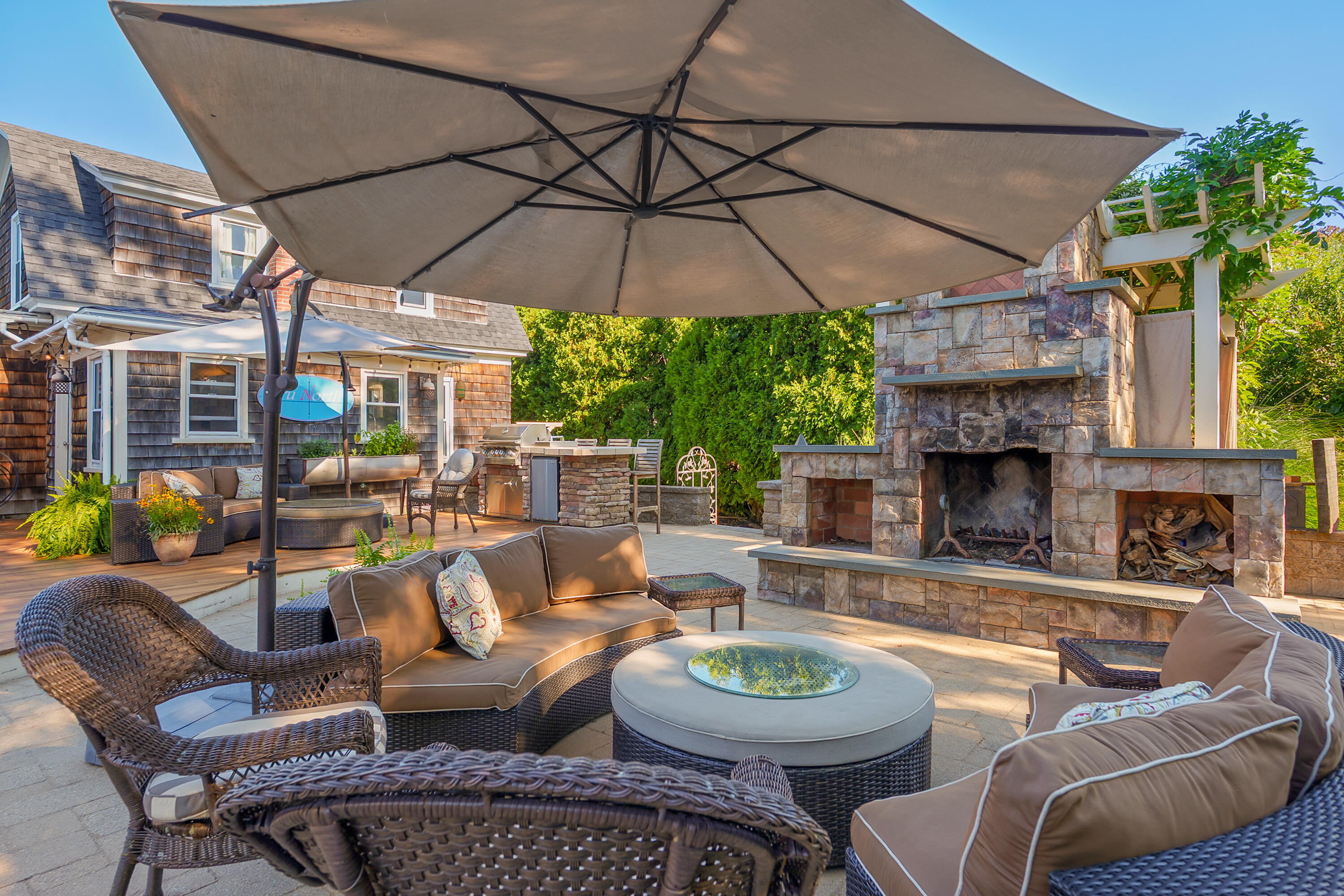 Outdoor patio with wicker seating, a large umbrella, and a stone fireplace.