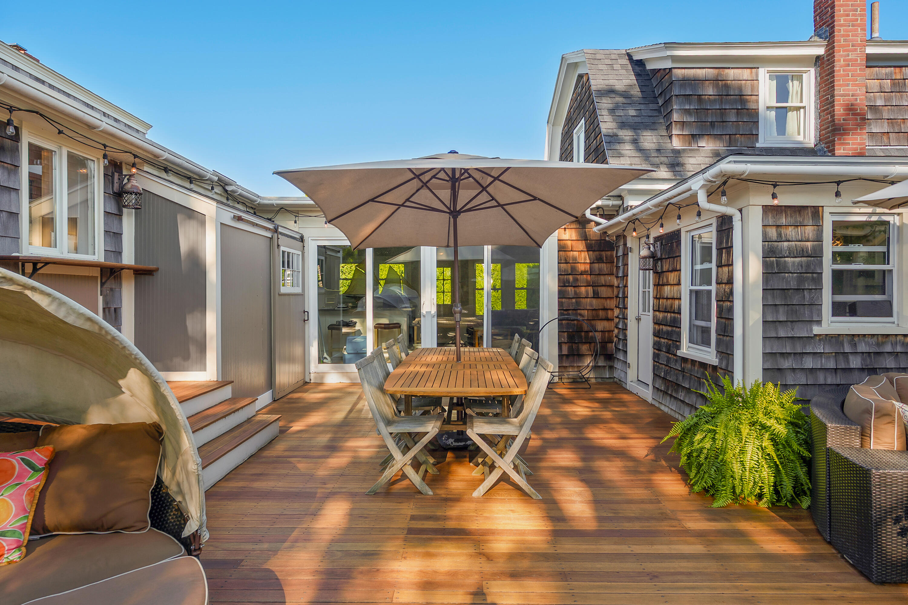 Wooden patio deck with umbrella-covered dining table, lounge seating, and glass doors to the home.