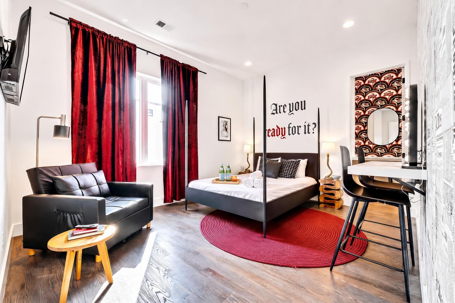 Furnished bedroom with a four-poster bed, deep red curtains, and a round red rug.