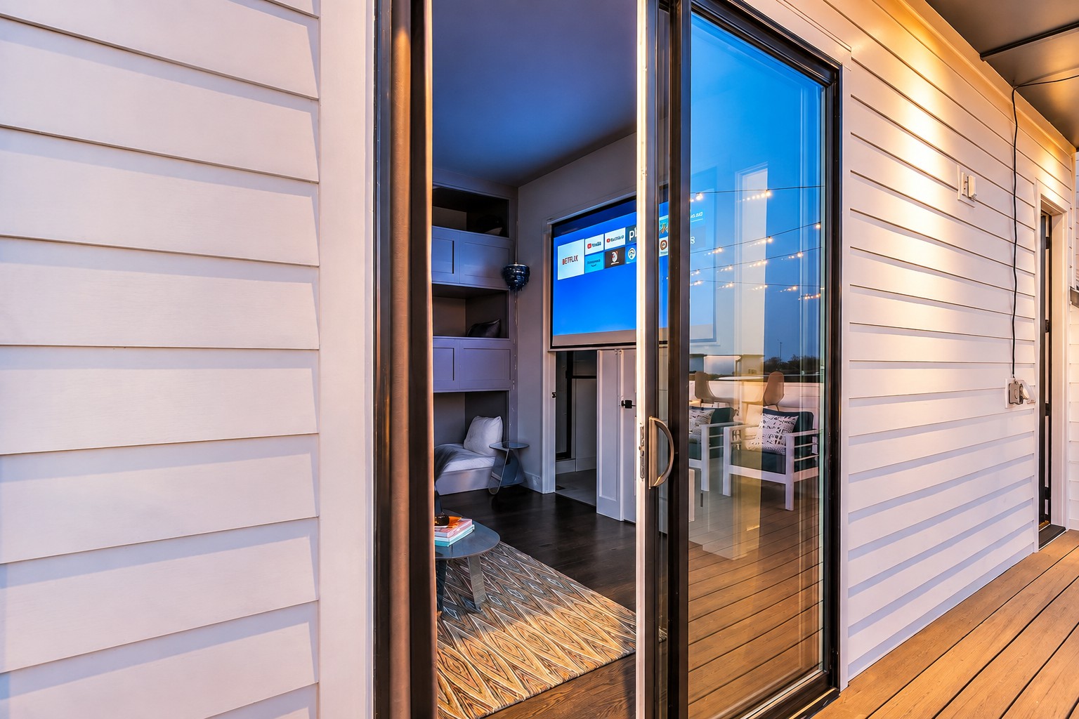 Wooden deck outside a sliding glass door, with a built-in sleeping nook and television inside.