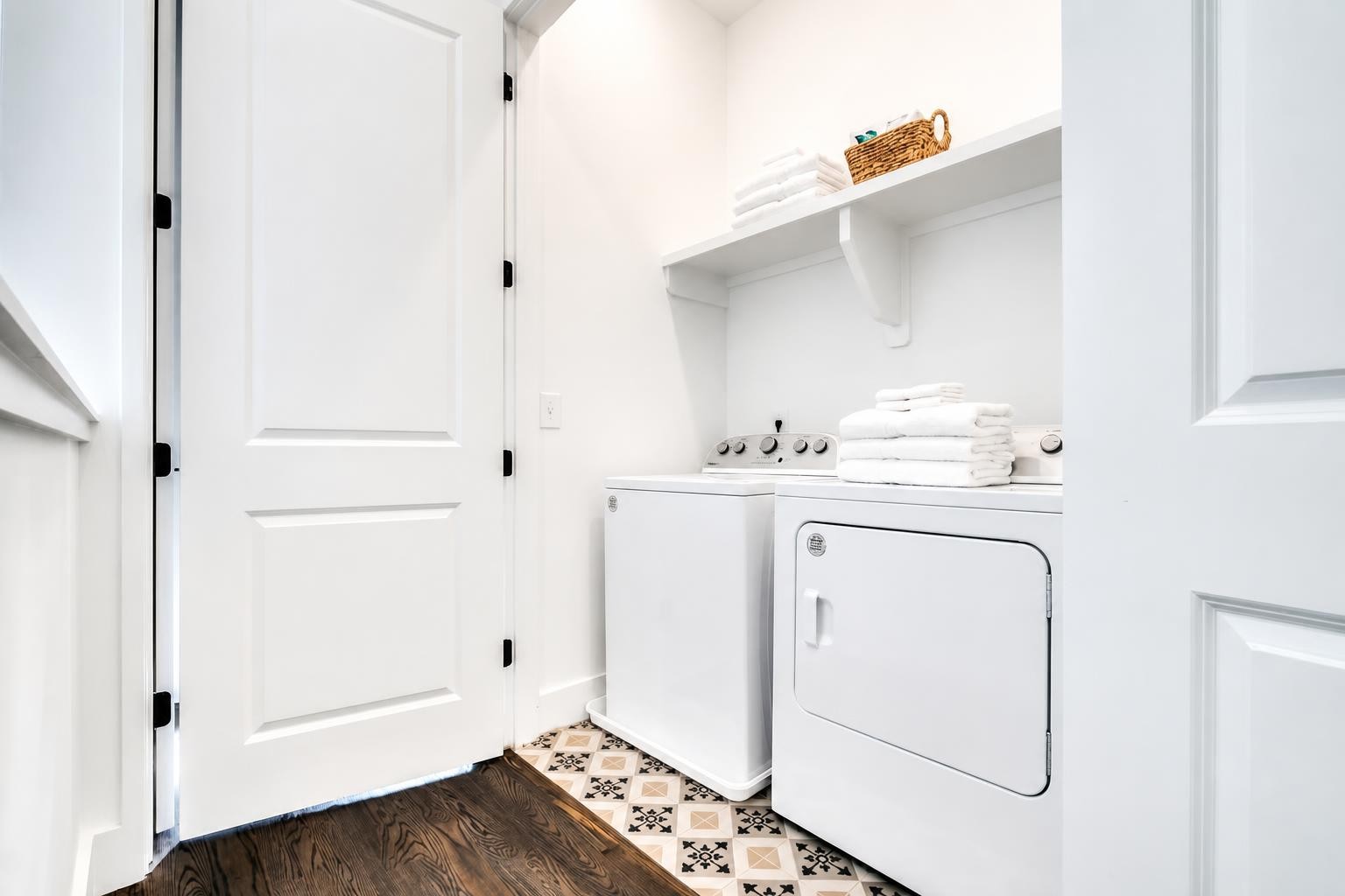 Laundry room with white washer and dryer, folded towels, and patterned tile floor.