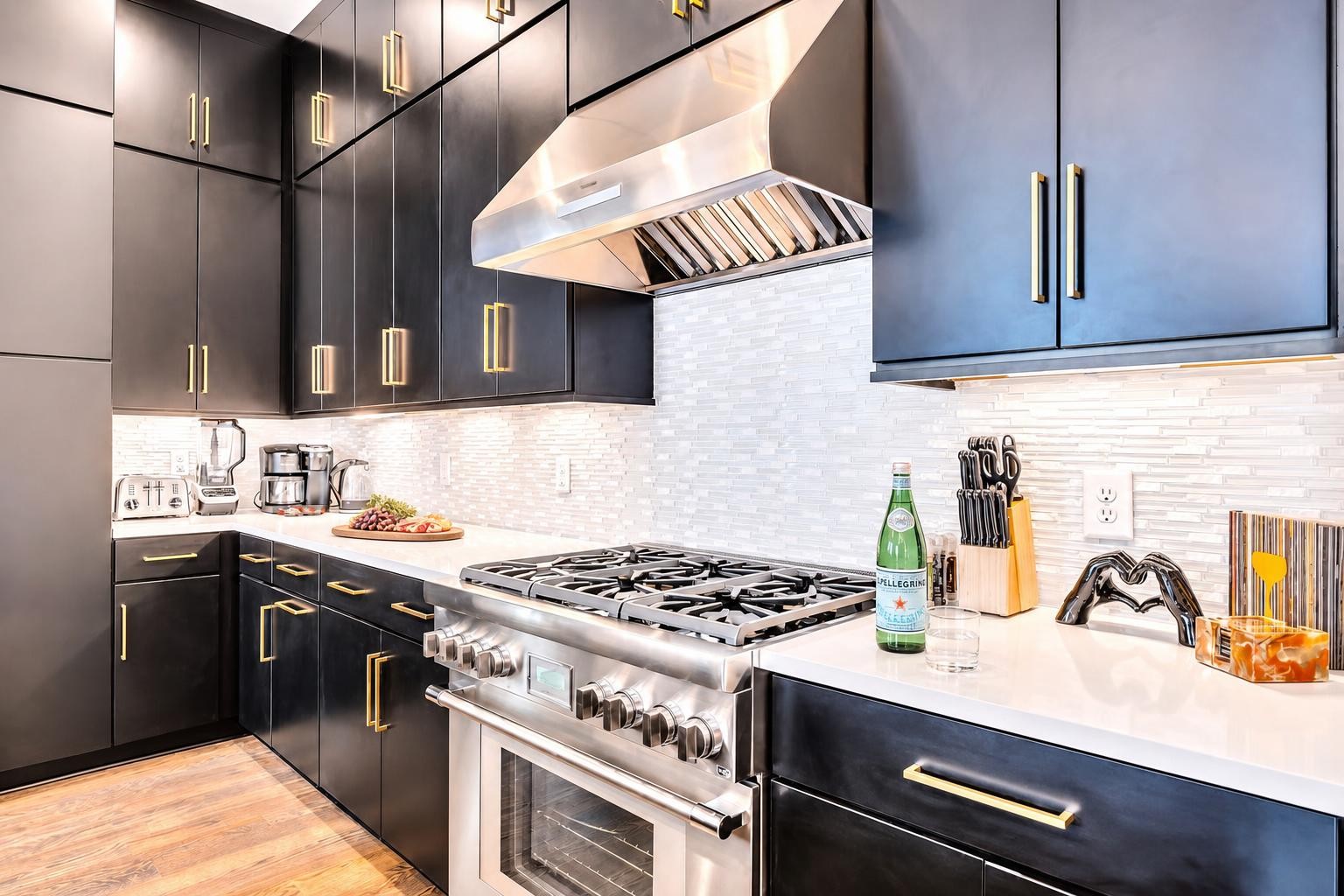 Modern kitchen with charcoal cabinets, brass pulls, and a prominent stainless-steel range and hood.