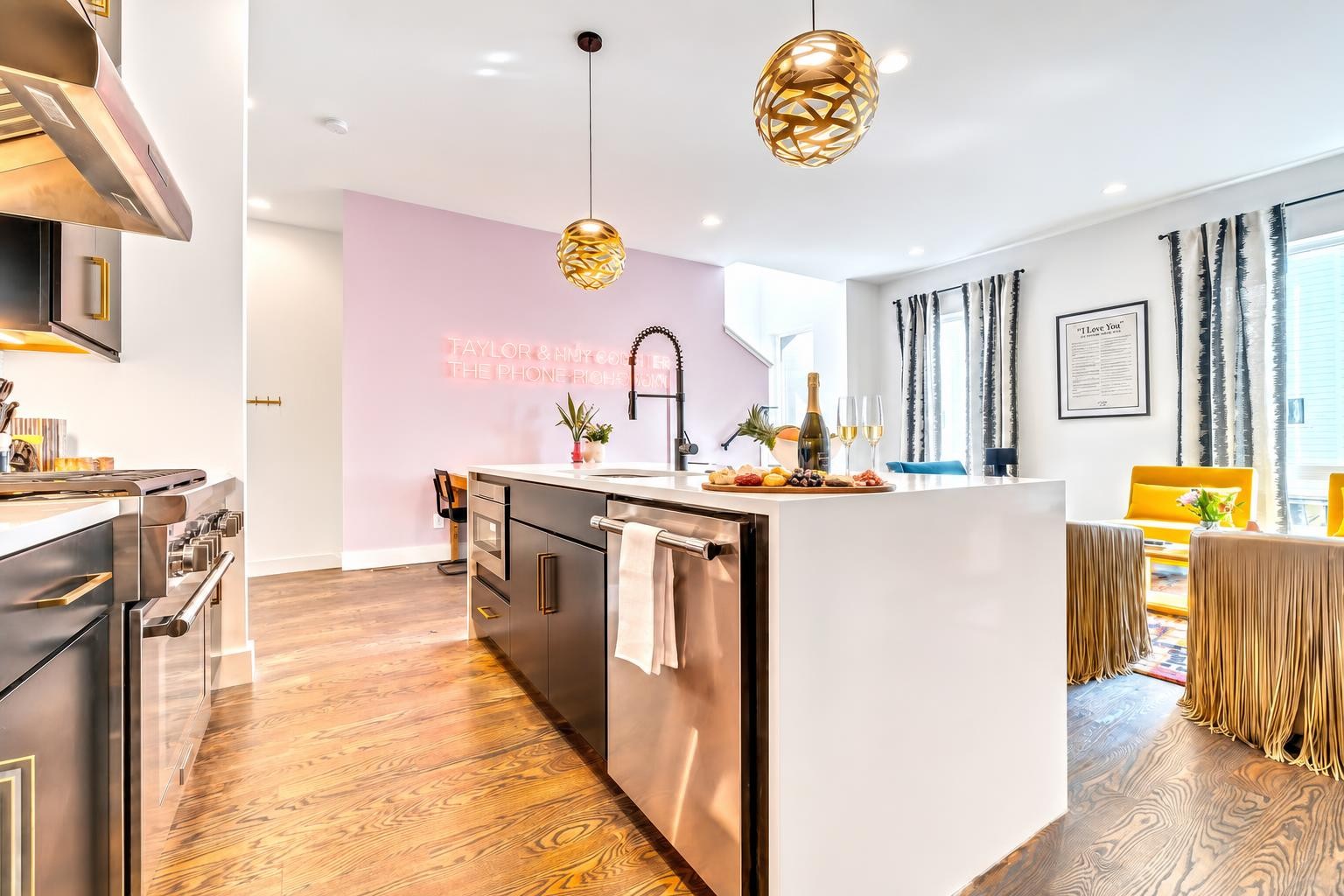 Staged kitchen with a large white island, gold pendant lights, and a pink accent wall.