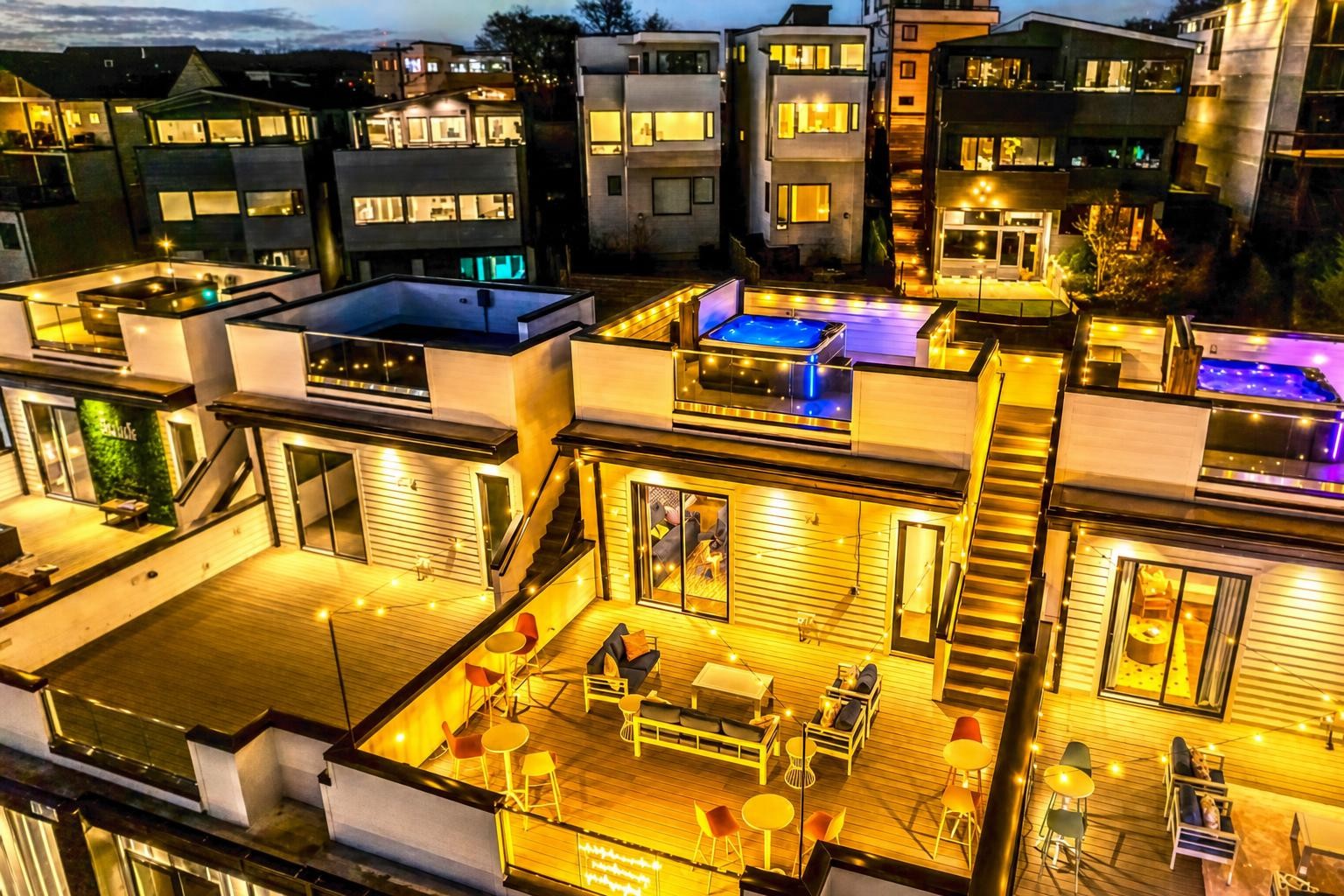 Modern homes with illuminated rooftop decks, outdoor seating, and hot tubs at night.