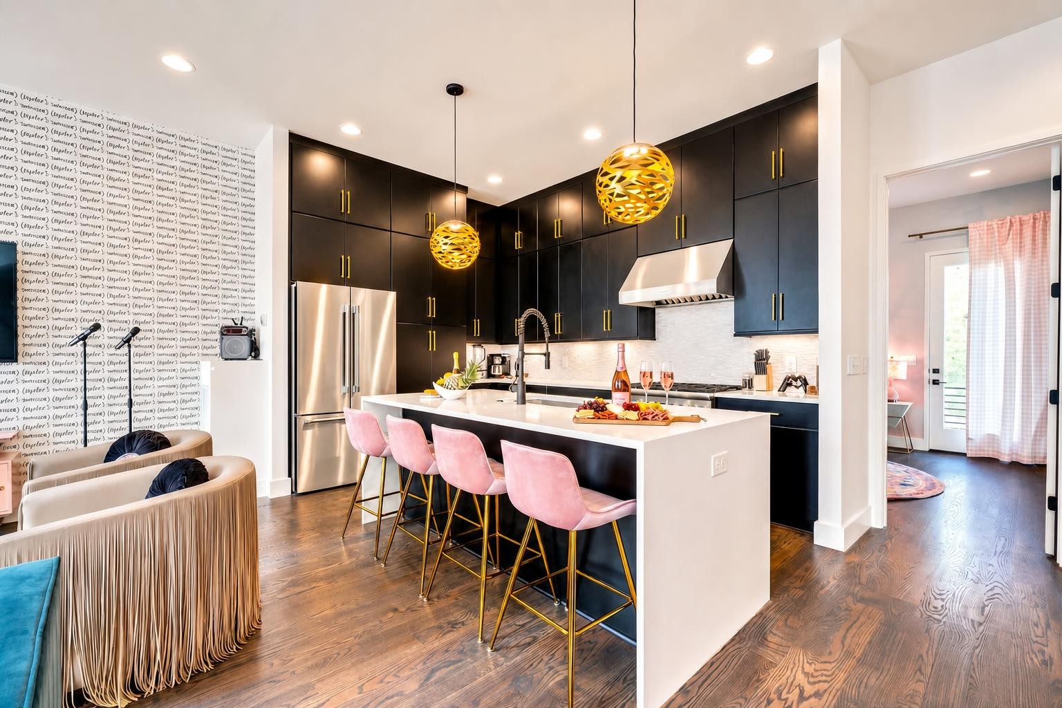 Modern kitchen with black cabinets, white island, pink stools, and gold pendant lights.