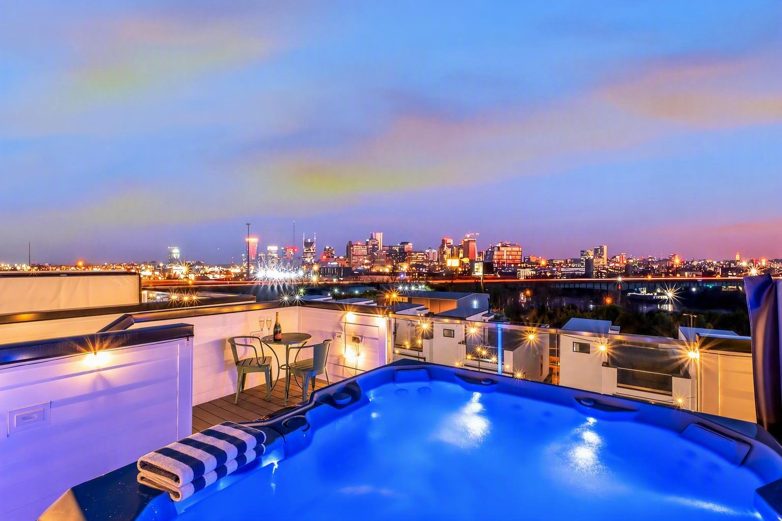 Rooftop hot tub overlooking the illuminated Nashville skyline, with an outdoor dining set beside it.