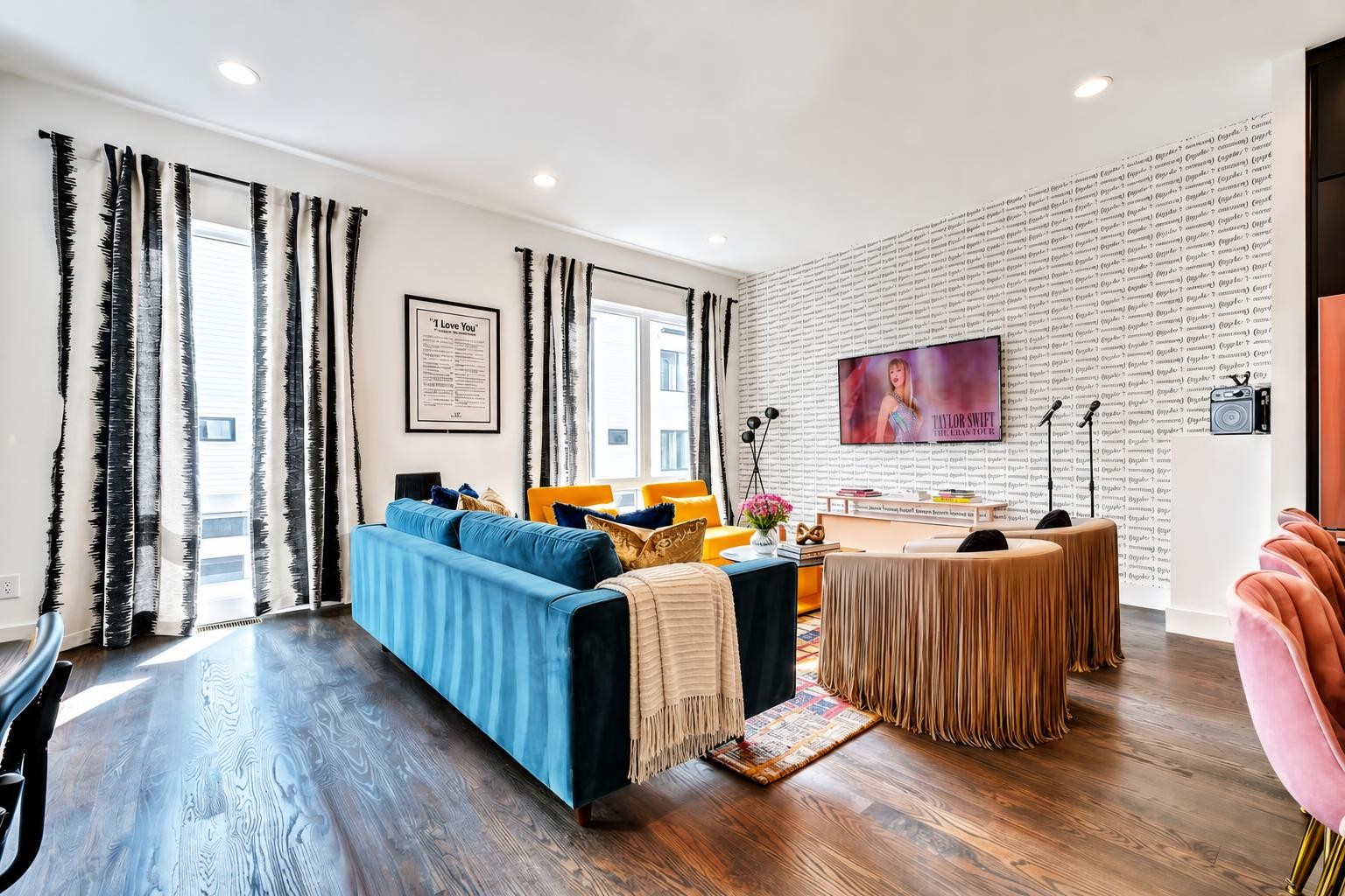 Living room with a blue sofa, orange chairs, and a round fringe-covered table against a text-patterned wall.