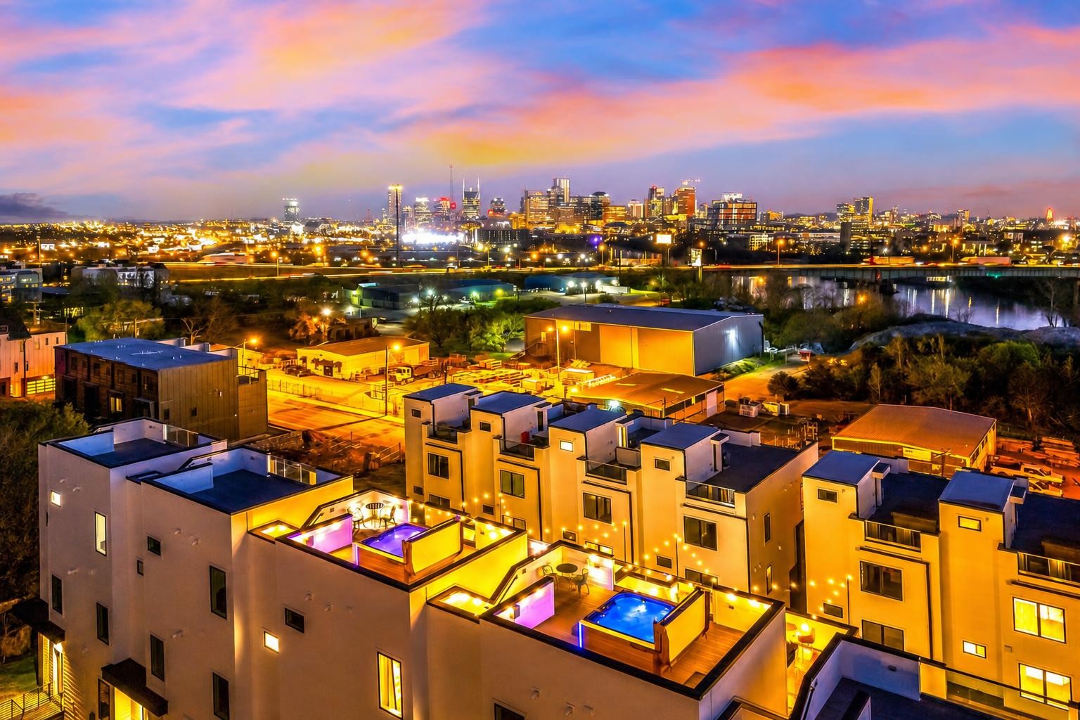 Modern townhomes with rooftop decks and pools overlook the Nashville skyline at dusk.
