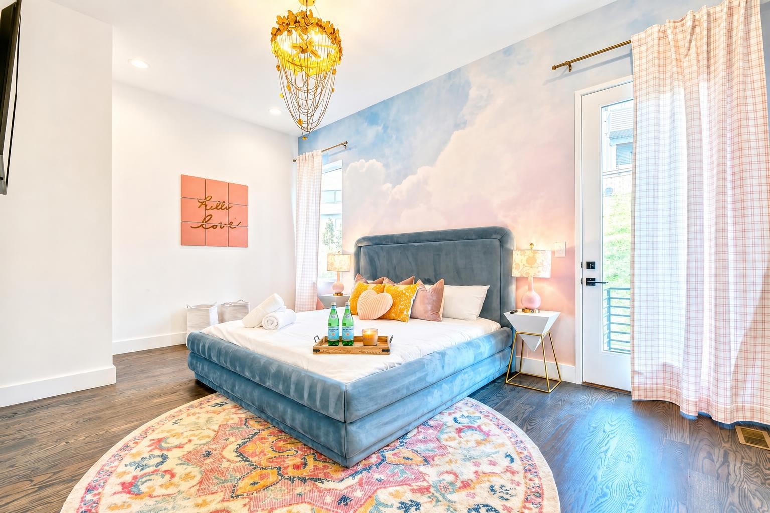 Bedroom with a blue upholstered bed, cloud mural, and colorful round rug.