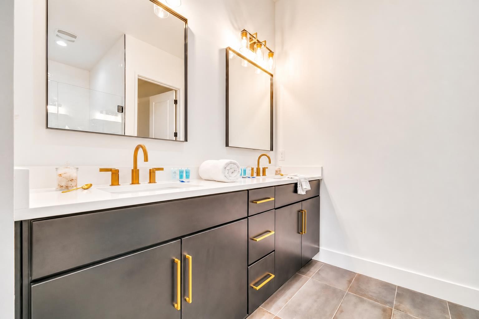 Modern double-sink bathroom vanity with gold faucets, dark cabinets, and large mirrors.