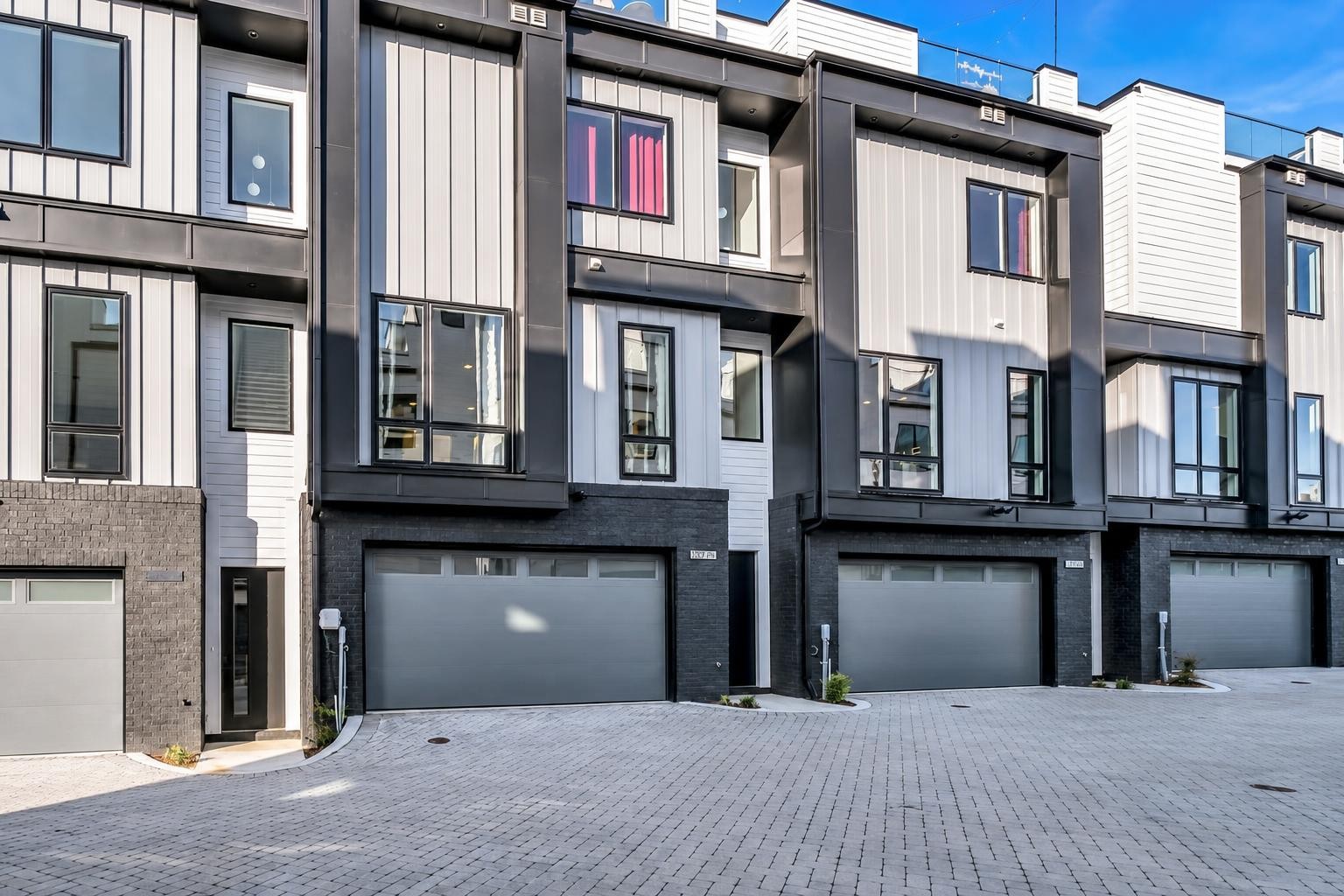 Modern row of townhomes with white siding, dark trim, and ground-level garages.