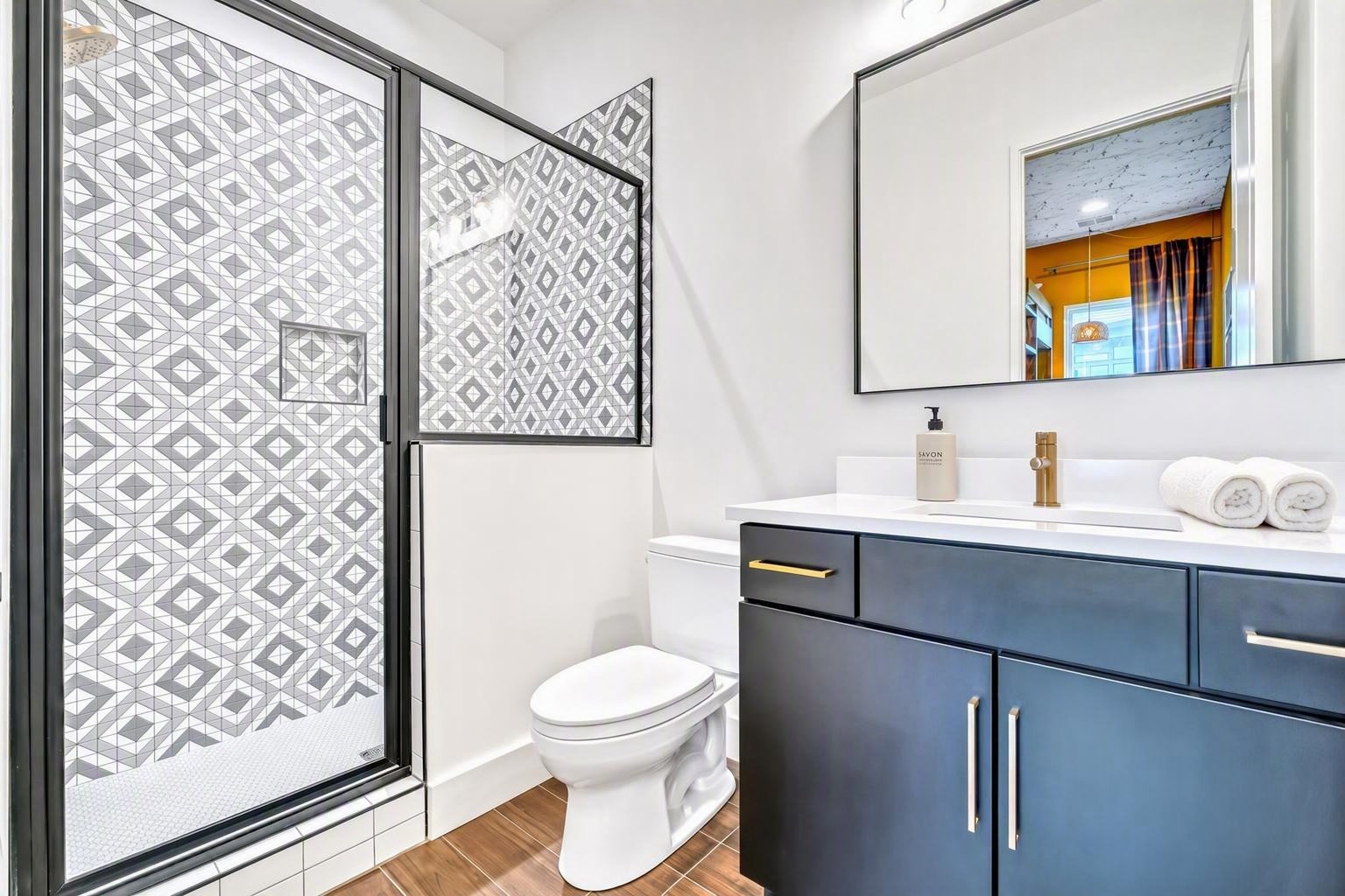 Bathroom with geometric tile shower, navy vanity, and gold fixtures.