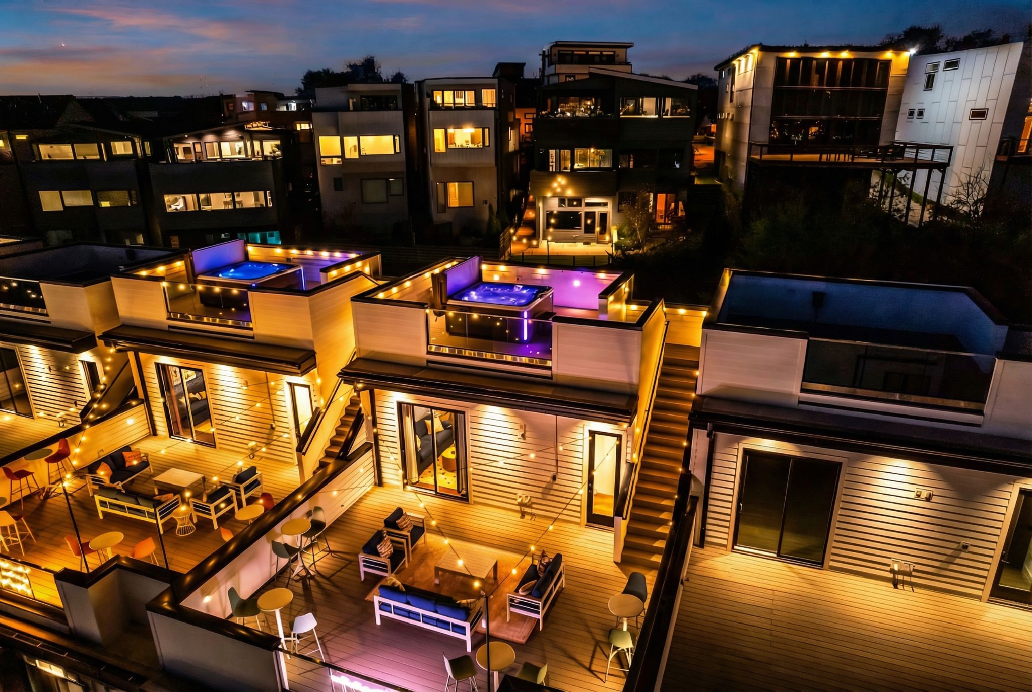 Modern homes with illuminated rooftop decks, outdoor seating, and pools at night.