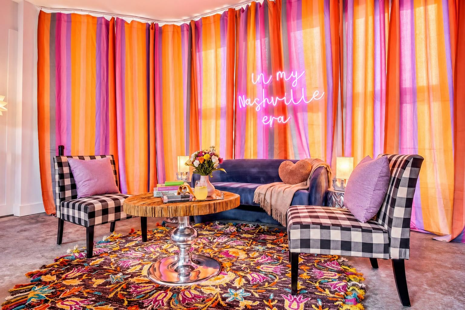 Staged living room with a navy sofa, checkered chairs, colorful rug, and “in my Nashville era” neon sign.