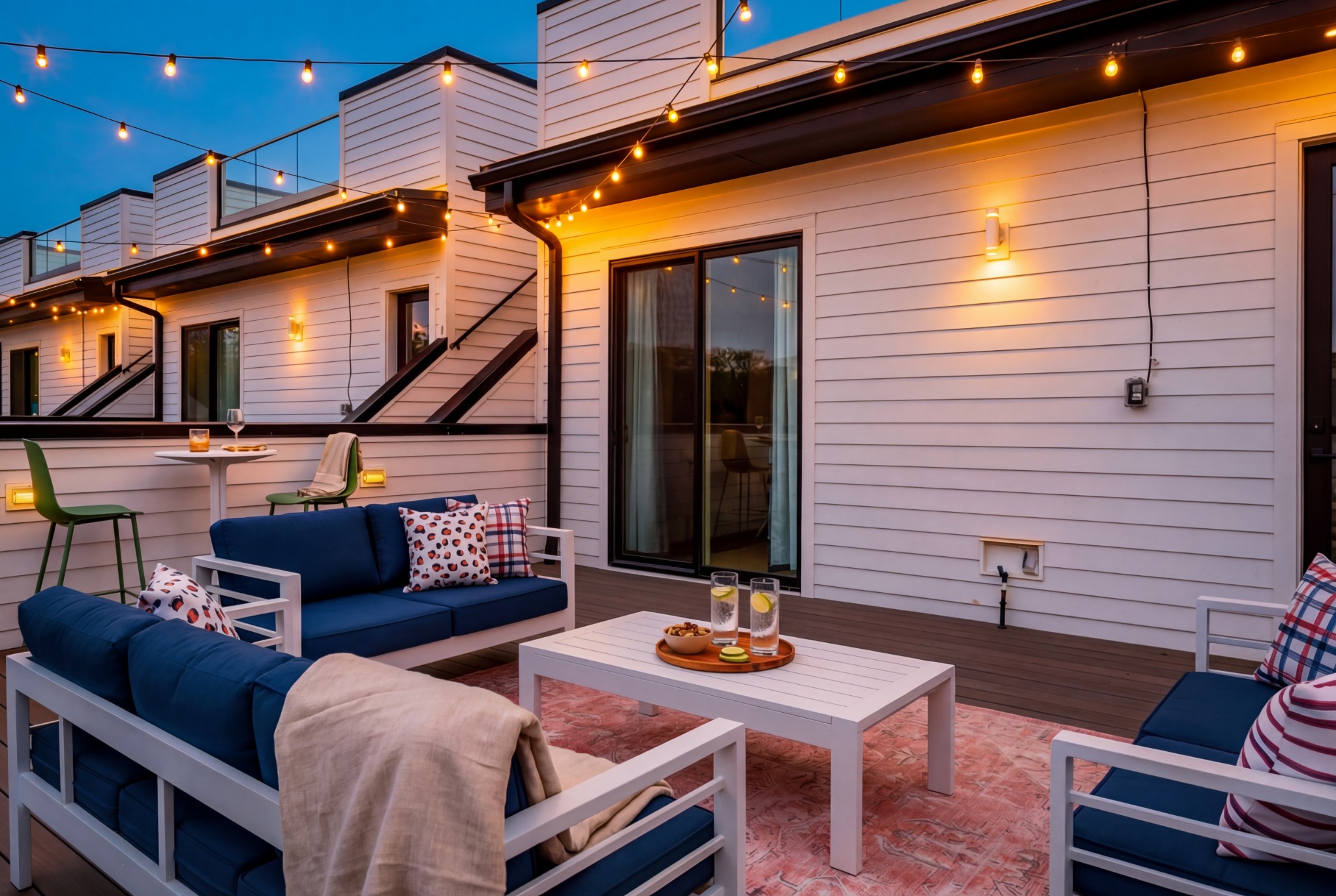 Rooftop deck with navy sofas, a white coffee table, and glowing string lights at dusk.