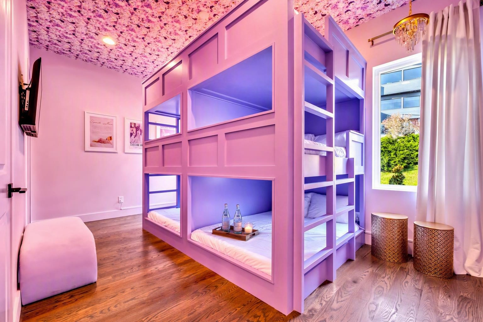 Bedroom with built-in pink bunk beds, floral ceiling, wood floors, and a window overlooking greenery.