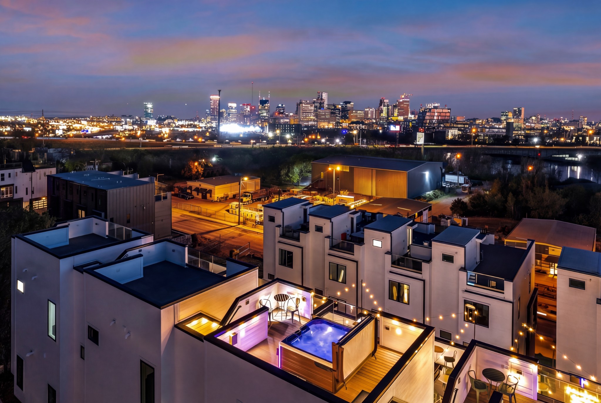 Modern townhomes with rooftop decks and a lit plunge pool overlooking the Nashville skyline at dusk.
