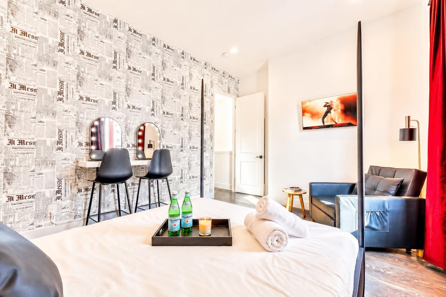 Furnished bedroom with newspaper-print wallpaper, a vanity, and a sitting area beside the bed.