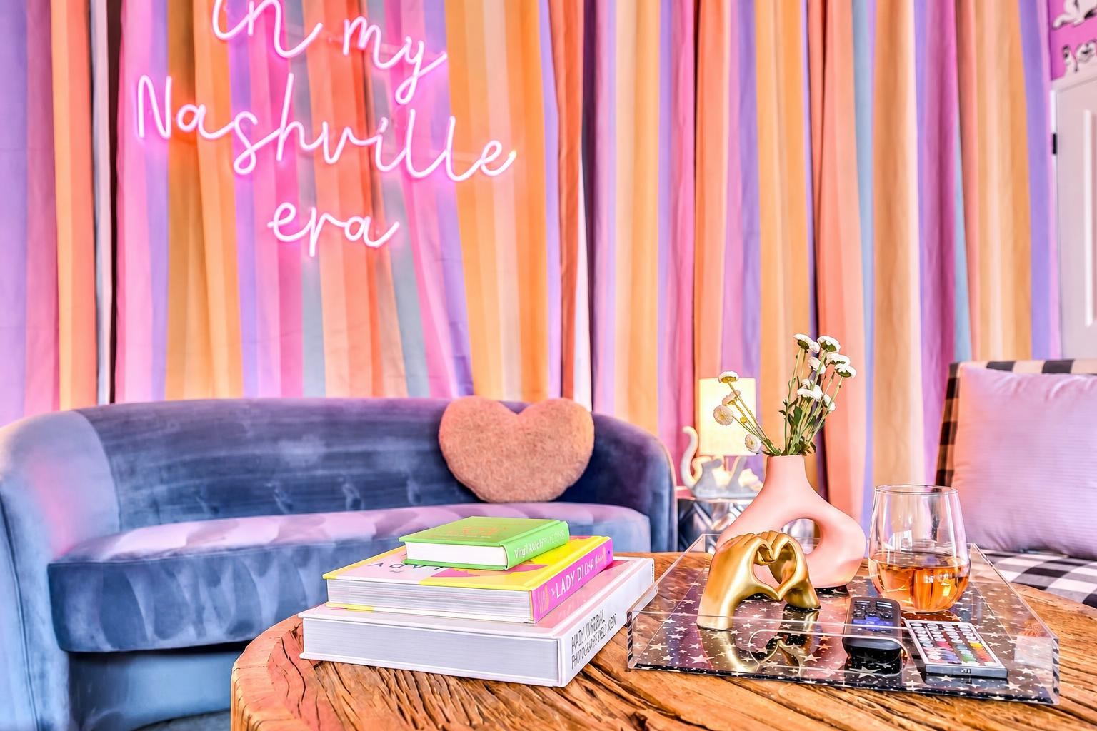 Colorful lounge with a blue velvet sofa, heart cushion, and “In my Nashville era” sign.