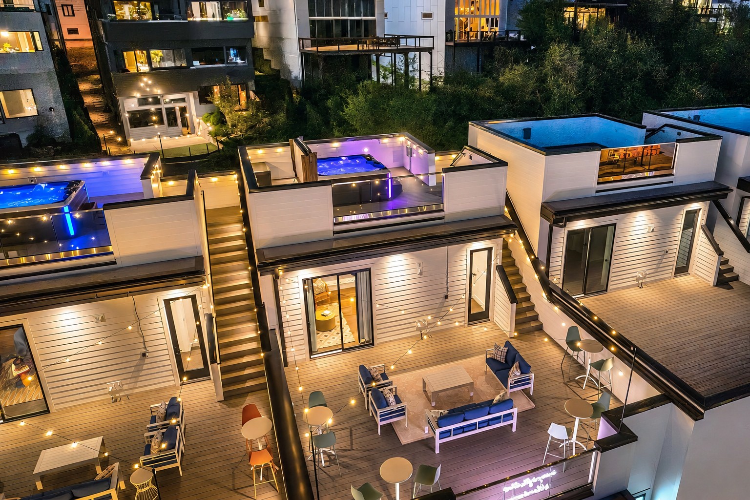 Modern rooftop decks with illuminated hot tubs, outdoor seating, and string lights at night.