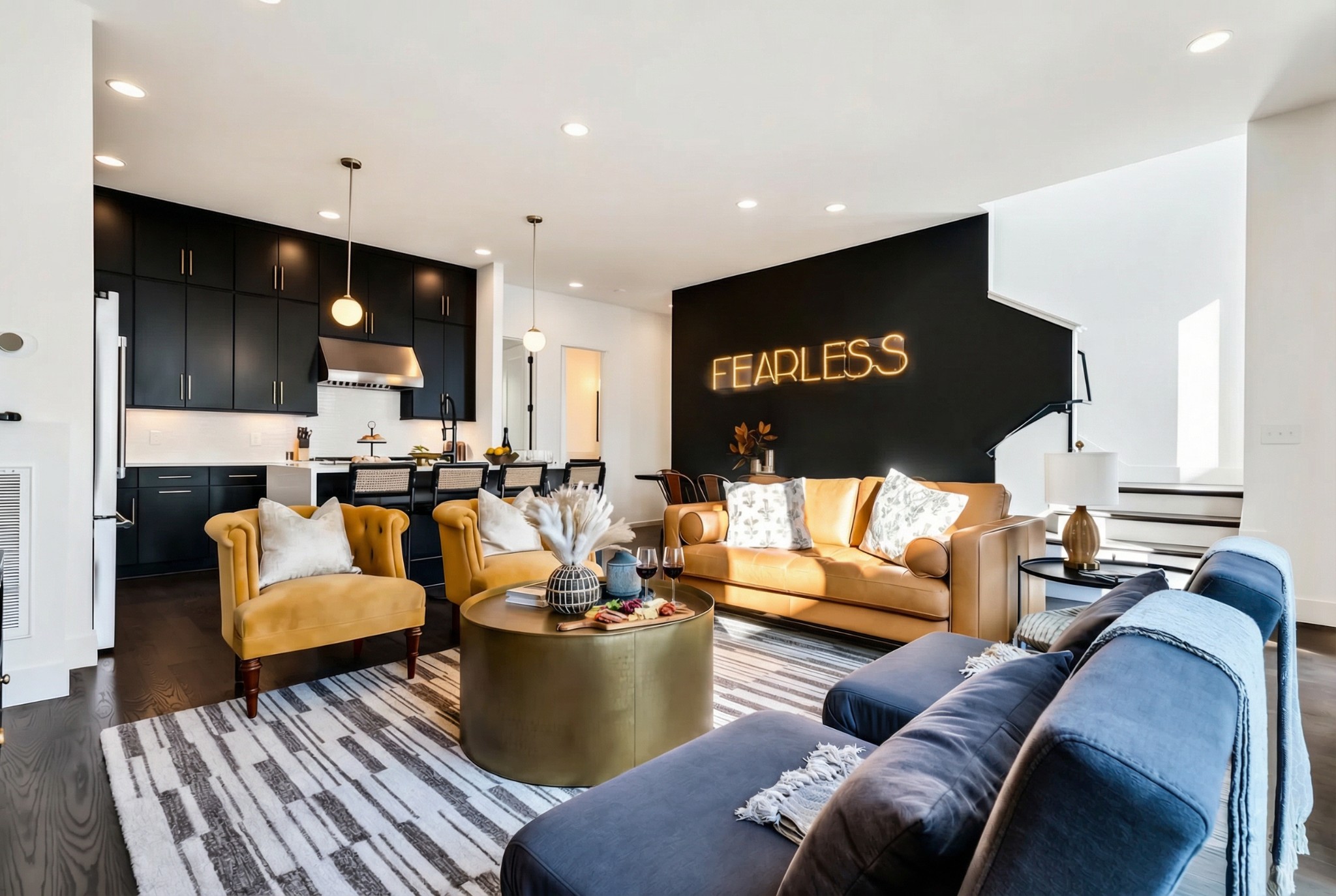 Open-plan living room and kitchen with a blue sectional, mustard seating, and black cabinetry.