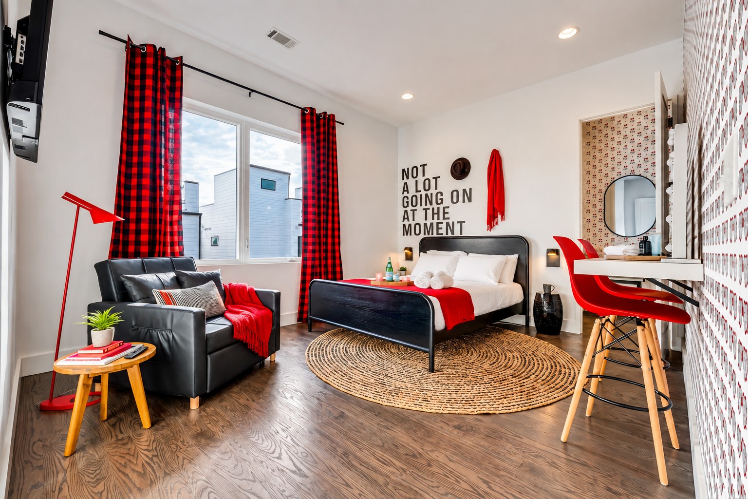 Furnished bedroom with a black bed, red accents, plaid curtains, and a sitting area beside the window.