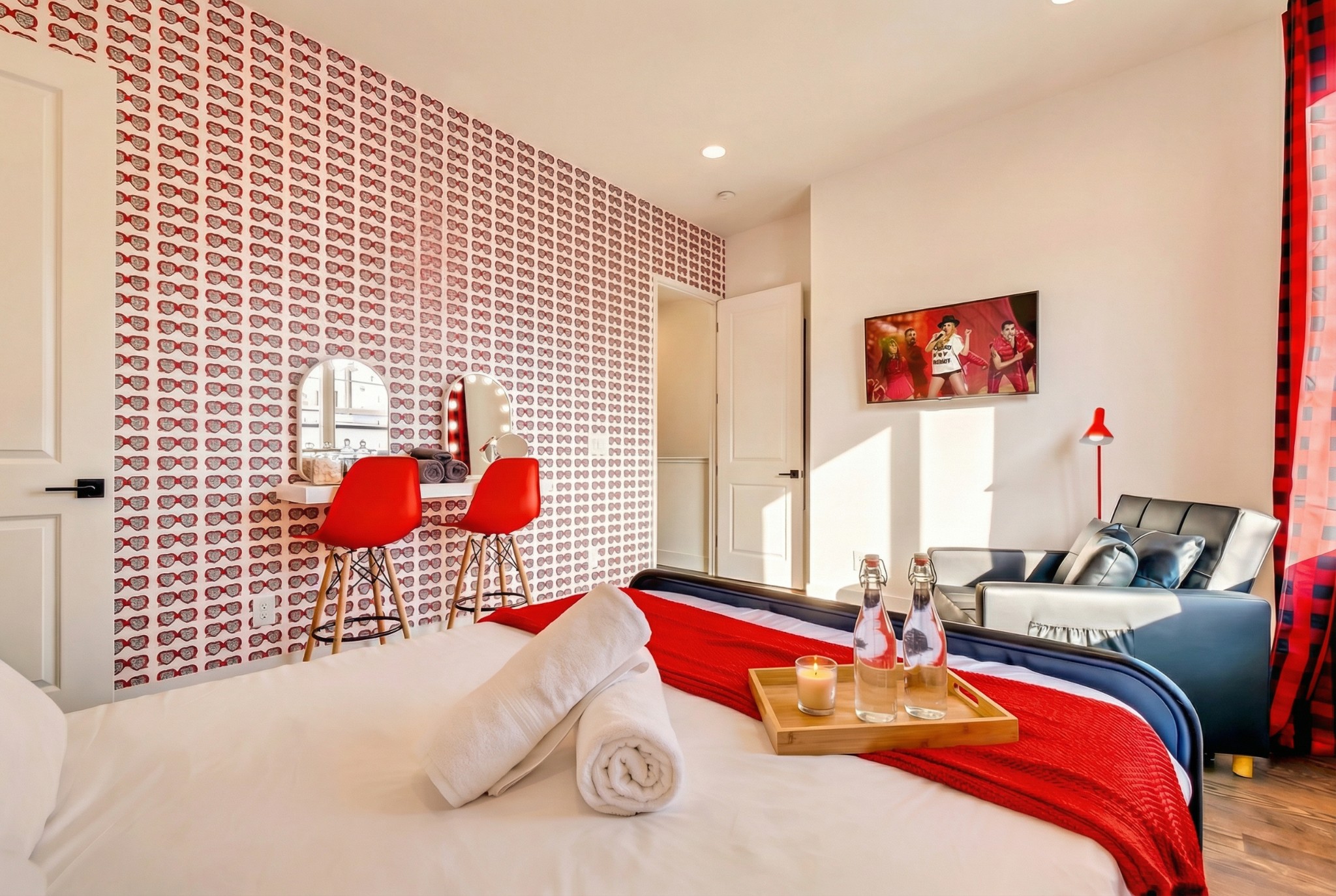 Bedroom with red-and-blue bedding, patterned wallpaper, a vanity, and a gray sofa.