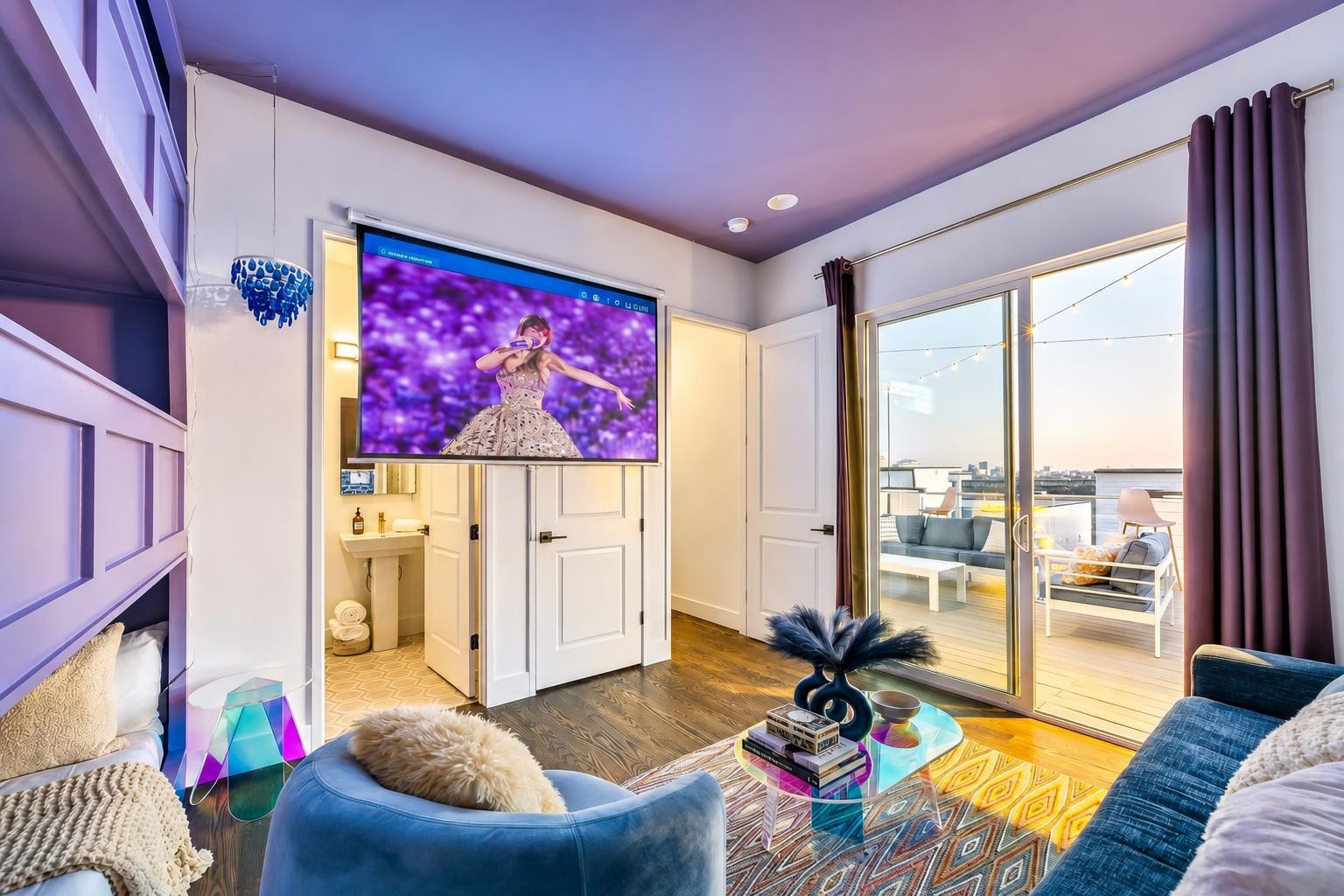 Living room with blue seating, colorful decor, and sliding doors to a balcony overlooking the city.