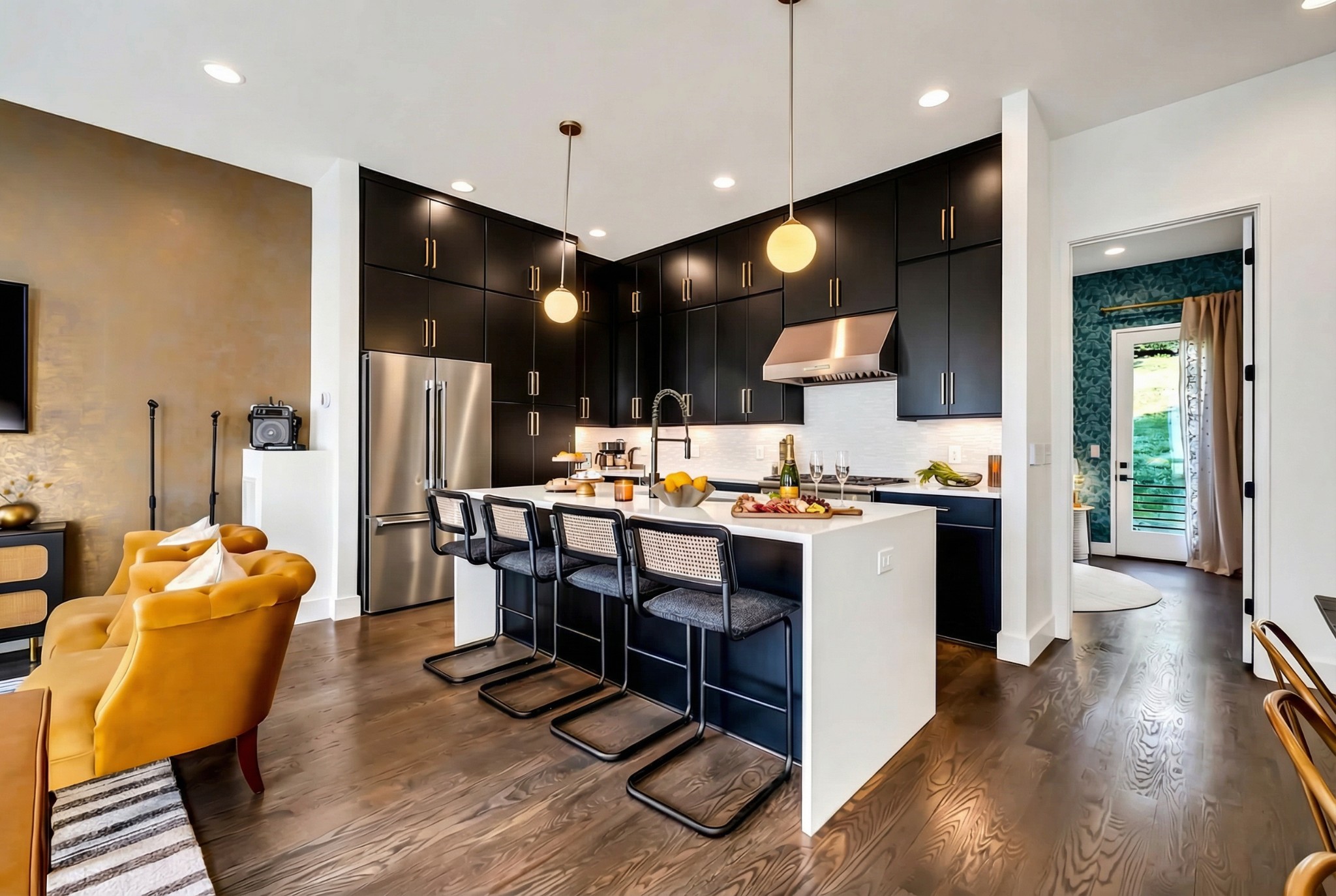 Open-plan kitchen with dark cabinets, a white island and four stools beside mustard-yellow seating.