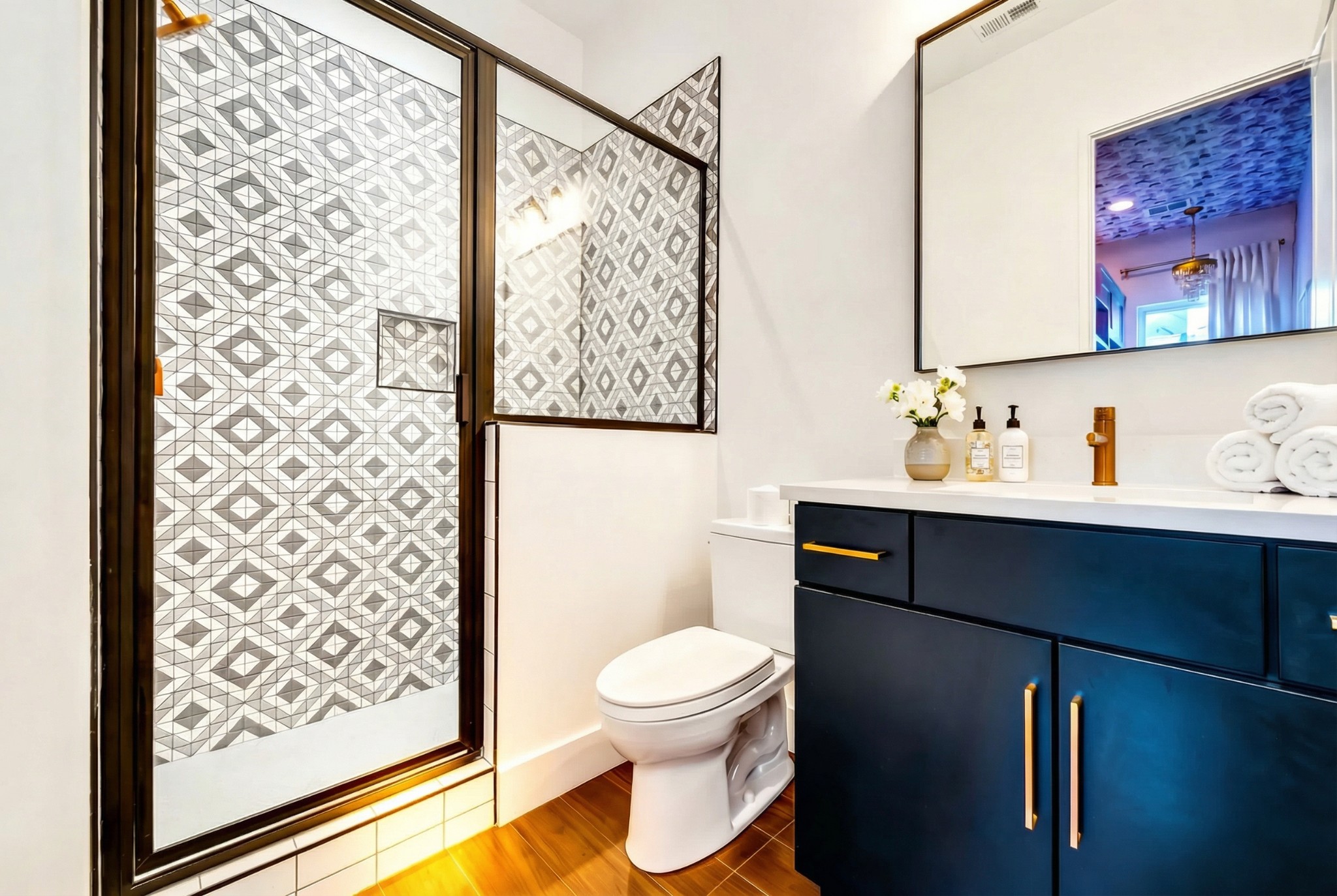 Bathroom with a geometric tiled shower and navy vanity with brass hardware.
