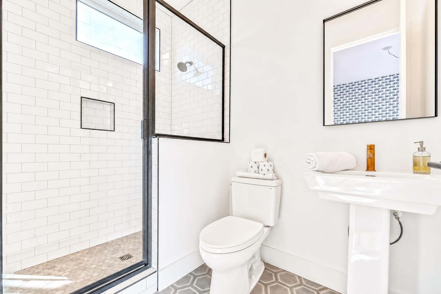 Bright bathroom with a glass walk-in shower, white subway tile, and gray geometric floor.