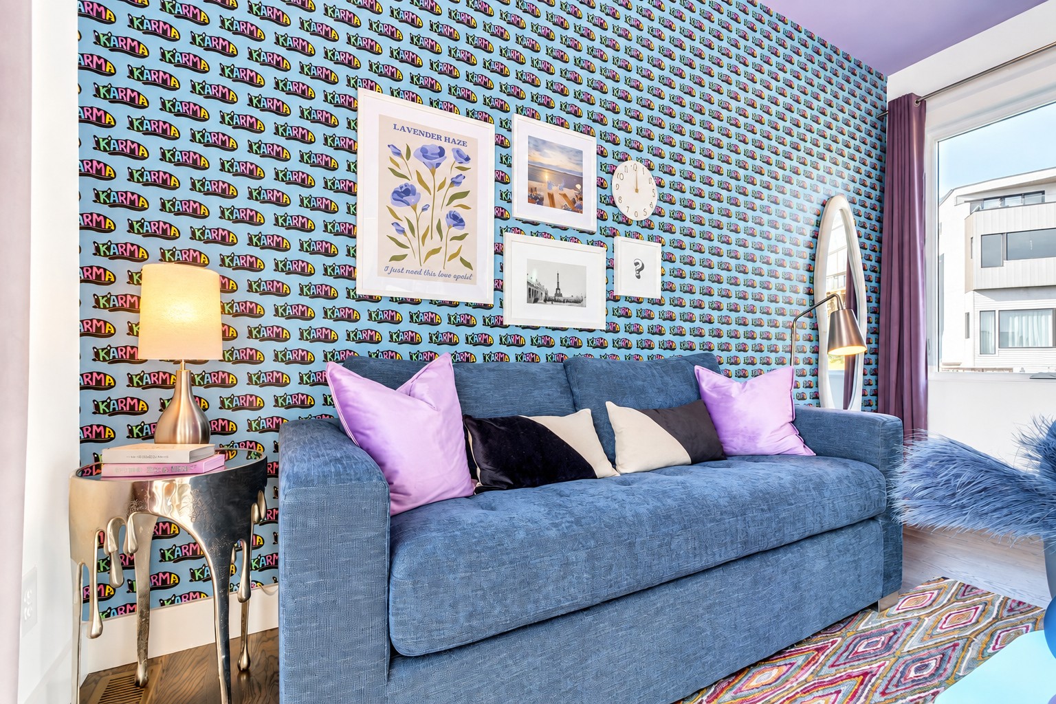 Living room with a blue sofa against colorful KARMA wallpaper and framed art.