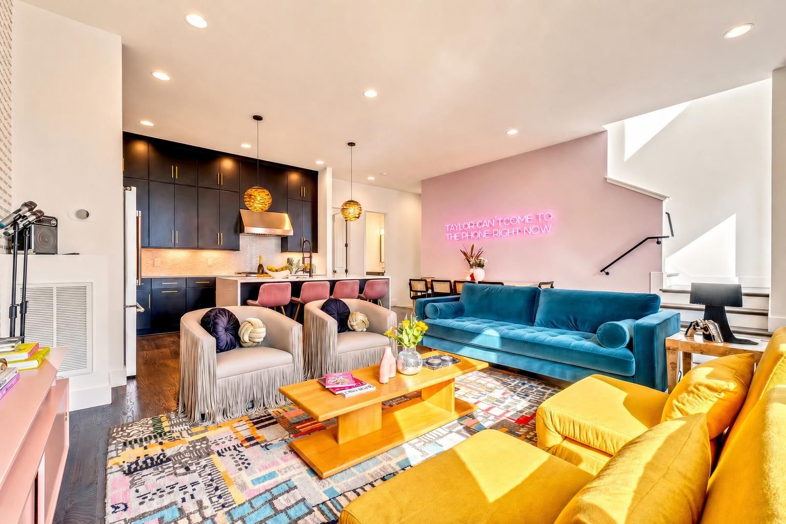 Open-plan living room with a turquoise sofa, yellow armchairs, and a neon sign above the dining area.