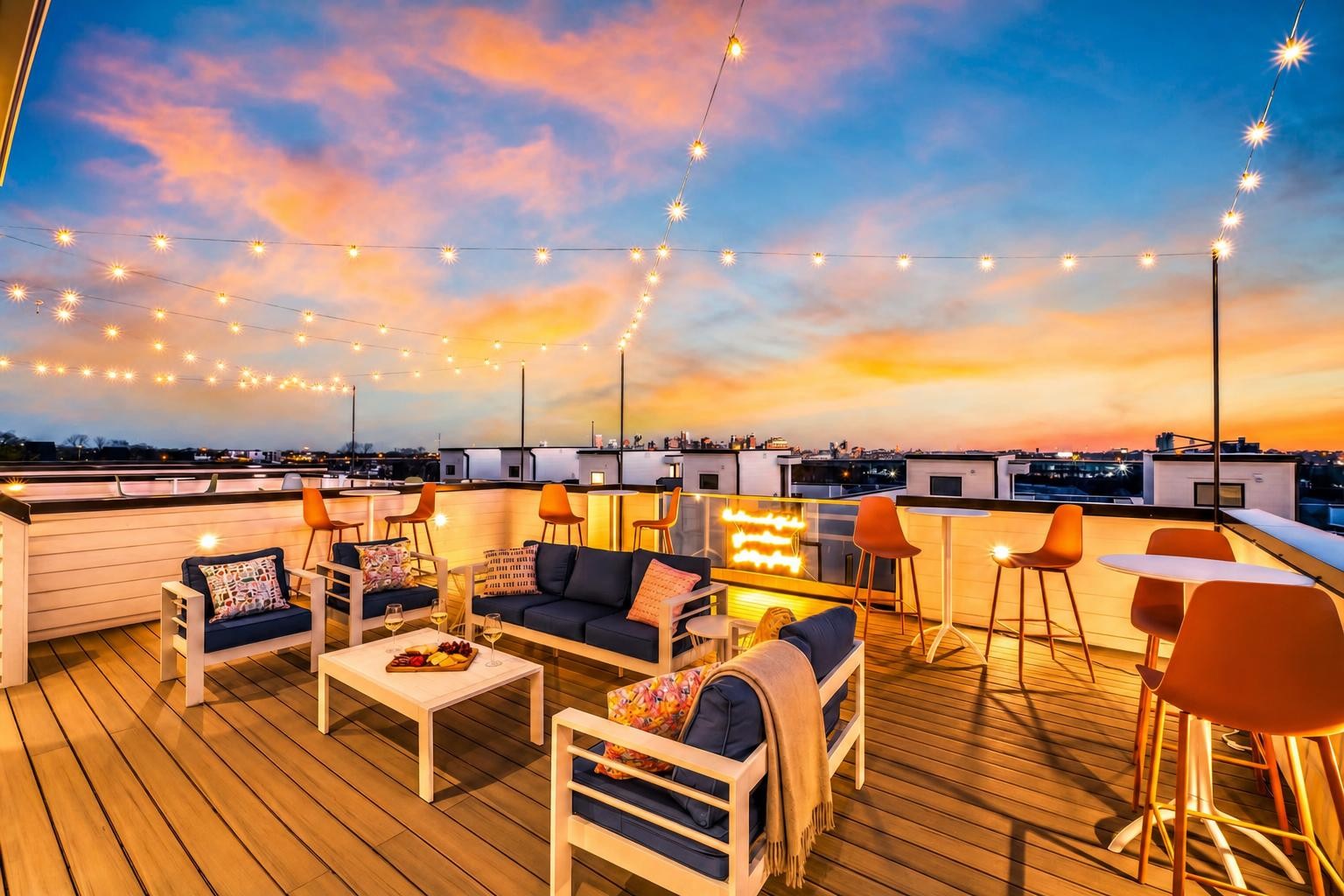Rooftop deck with lounge seating, string lights, and a fire feature overlooking the city at dusk.