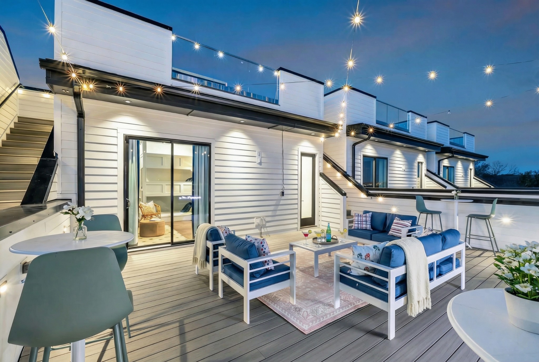 Furnished rooftop deck with blue seating and glowing string lights at dusk.