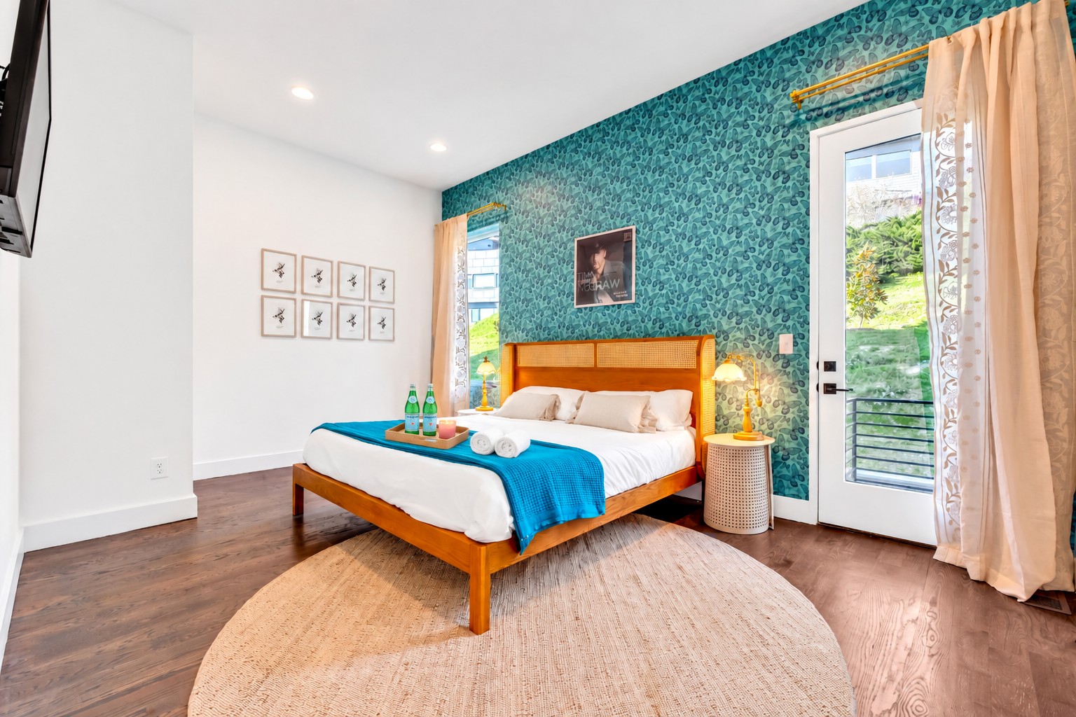 Bedroom with a wooden bed, teal patterned accent wall, and glass balcony door overlooking greenery.