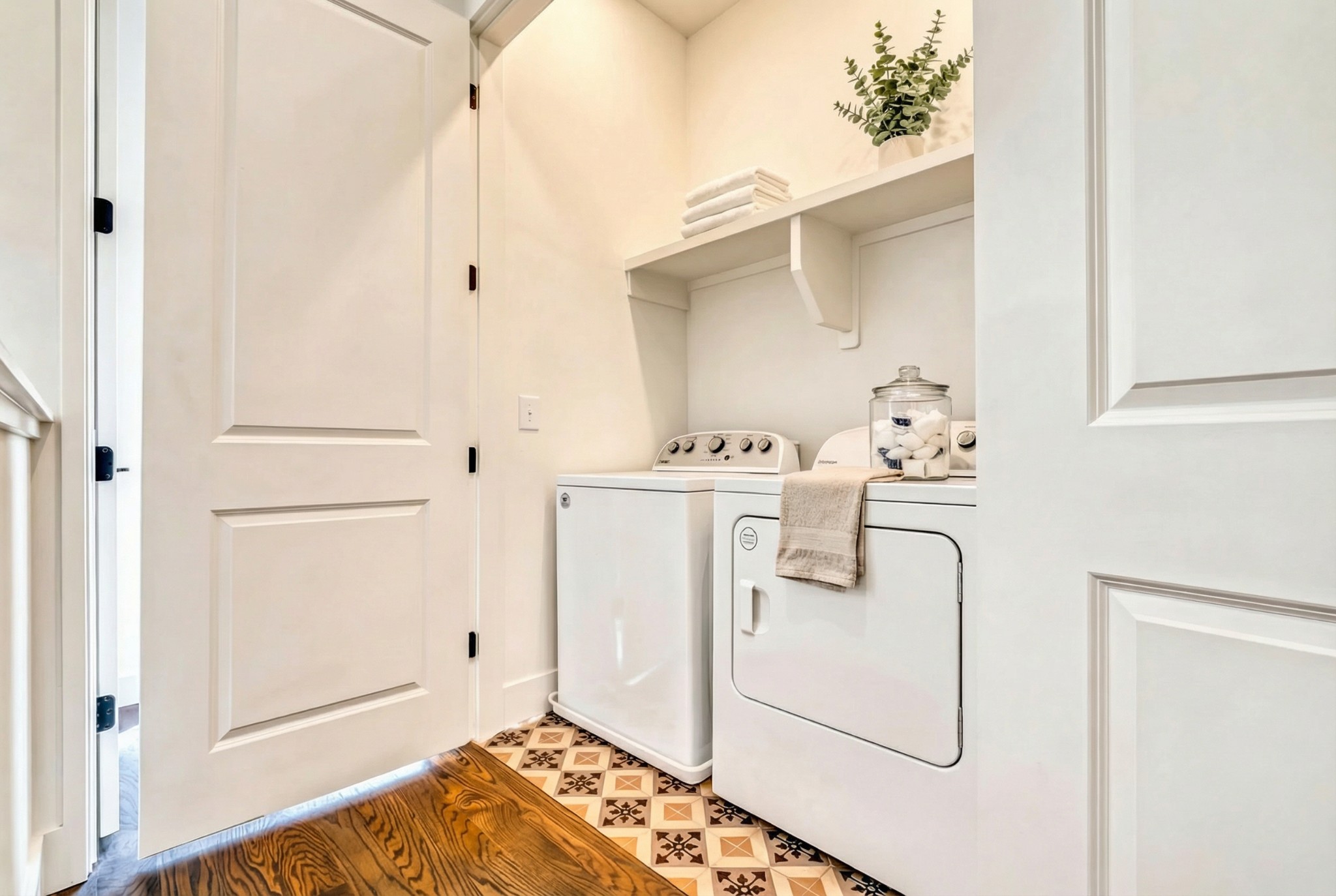 Laundry room with white washer and dryer, patterned tile flooring, and a shelf with folded towels.