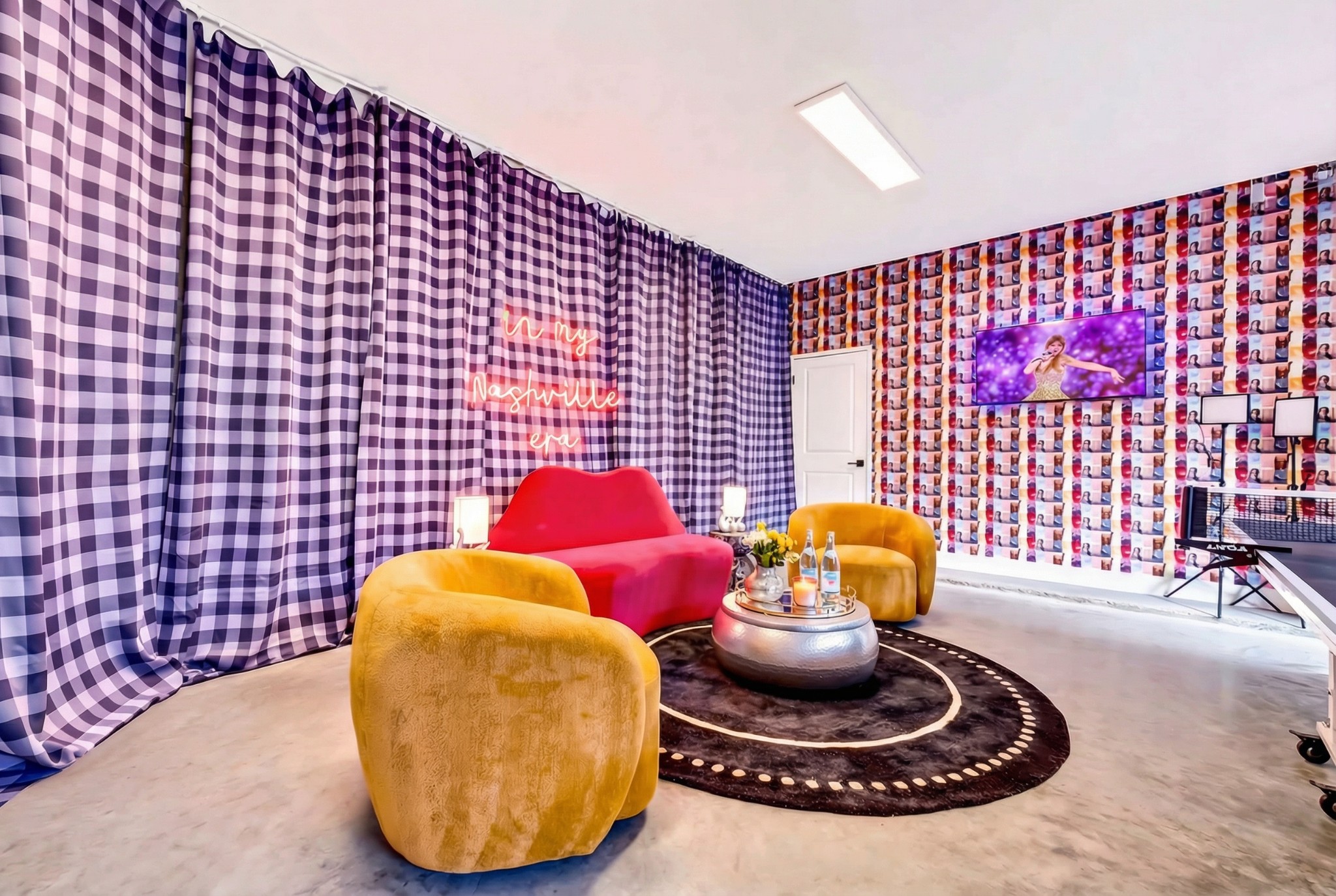 Colorful lounge with a pink sofa, mustard chairs, patterned walls, and a neon “in my Nashville era” sign.
