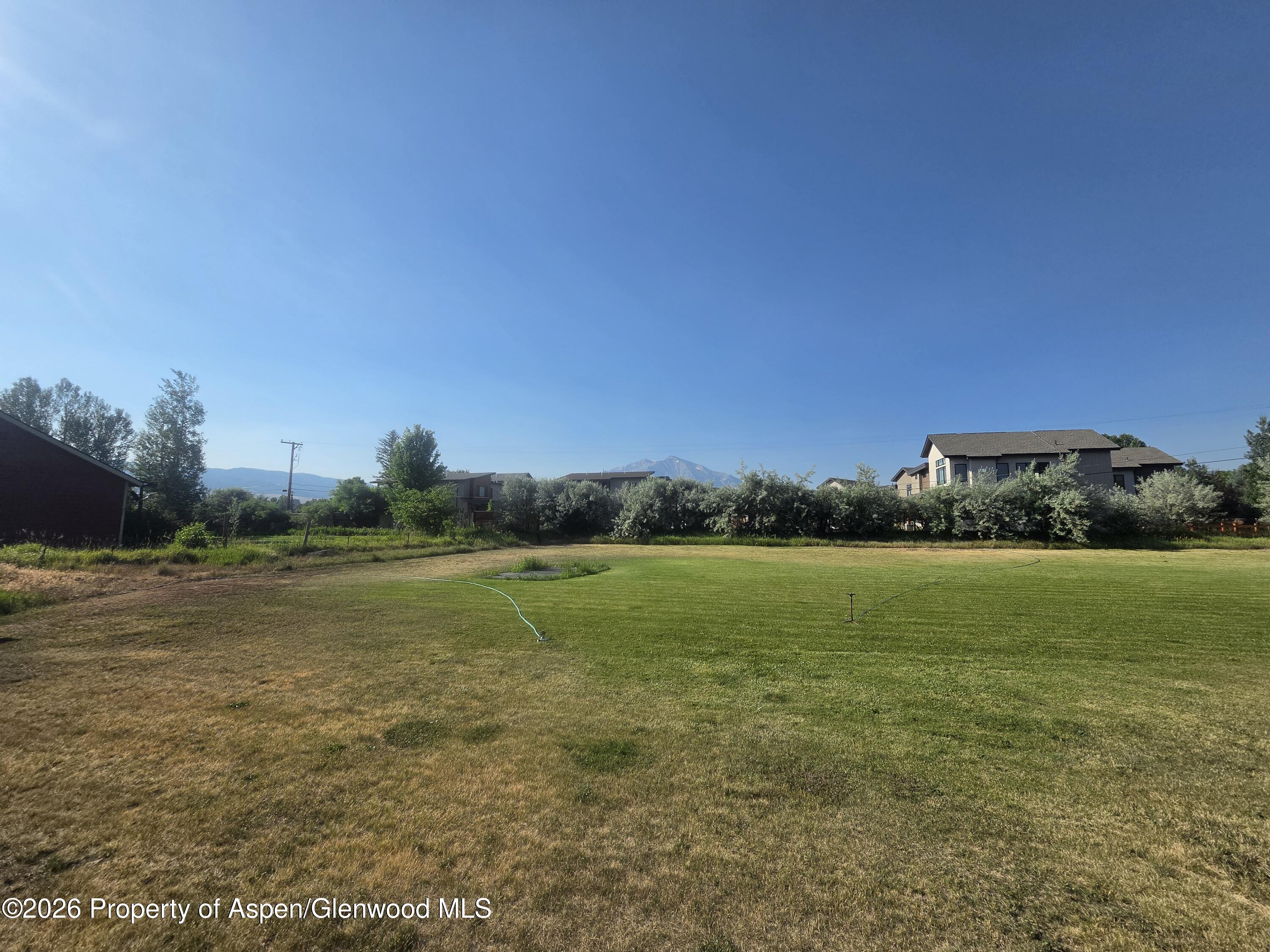 Grassy lot with an irrigation hose, neighboring homes, and mountain views.