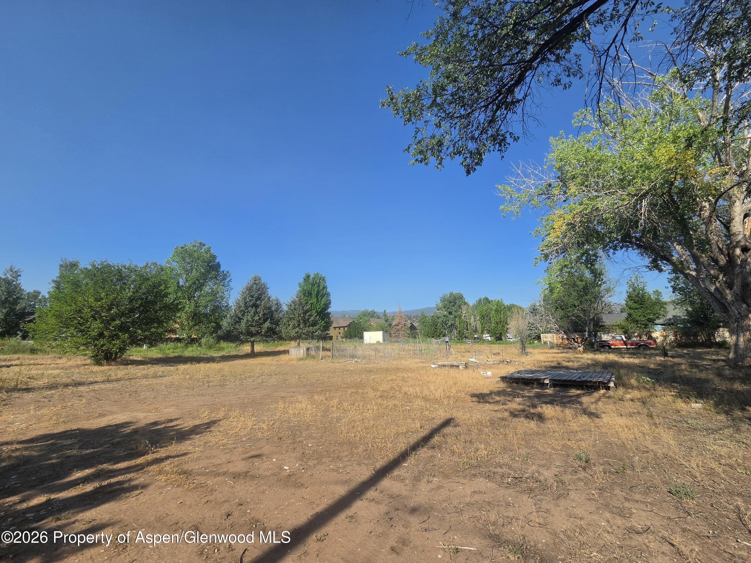 Open dry lot with mature trees, a fenced garden area, and a distant mountain ridge.