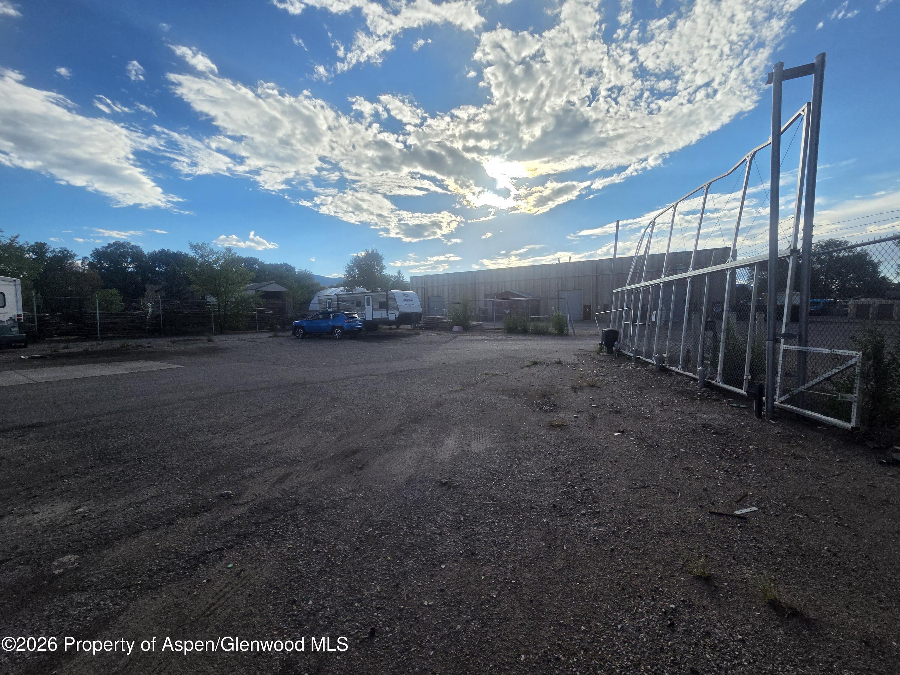 Gravel storage yard with chain-link fencing, a tall metal gate, and a parked travel trailer.