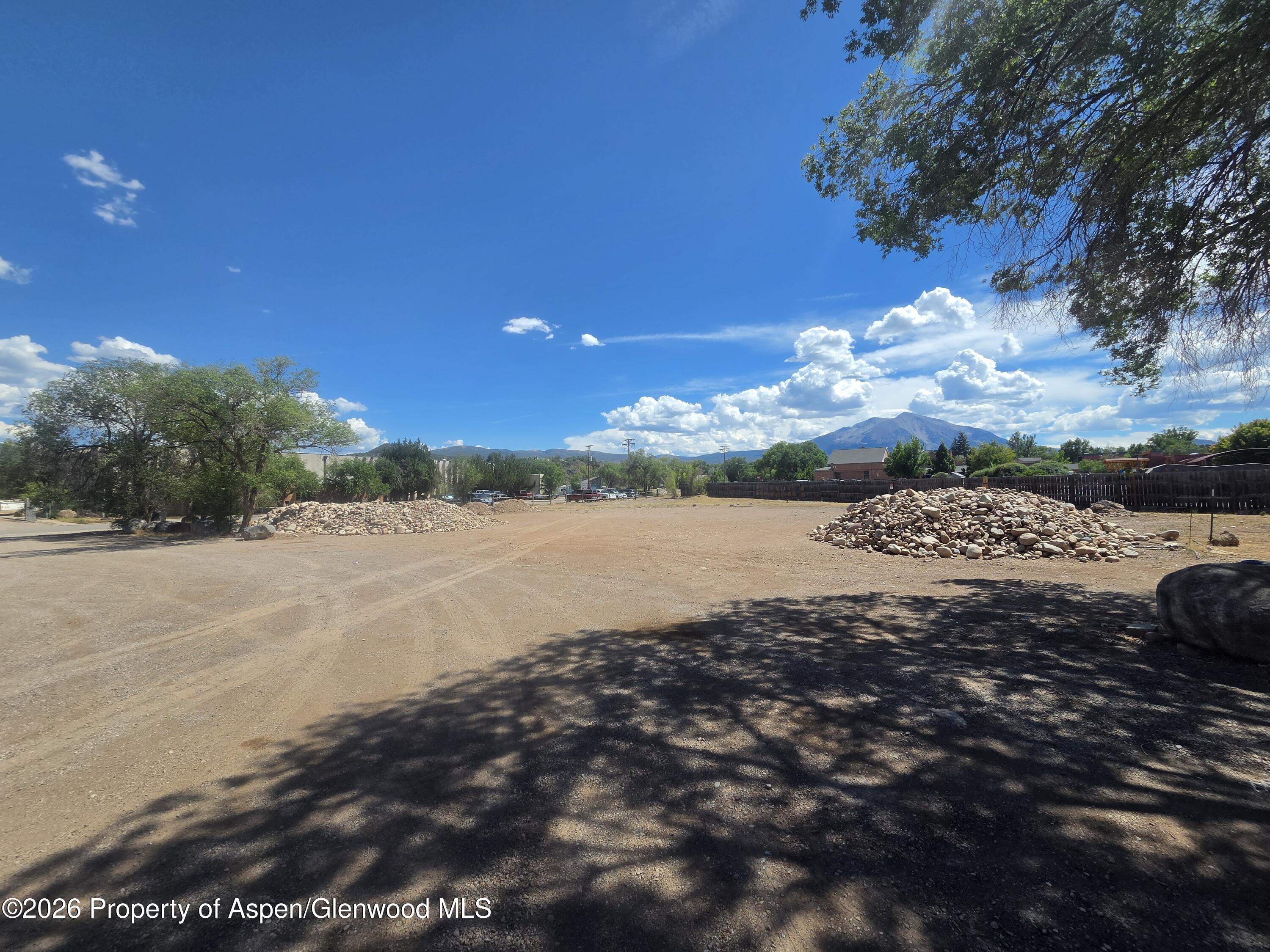 Open dirt yard with rock piles, trees, and mountain views.