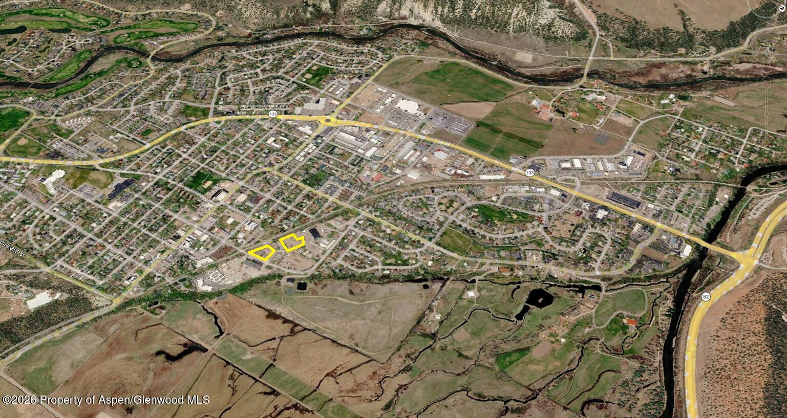 Aerial view of two outlined parcels amid Carbondale streets, commercial buildings, river, and open land.