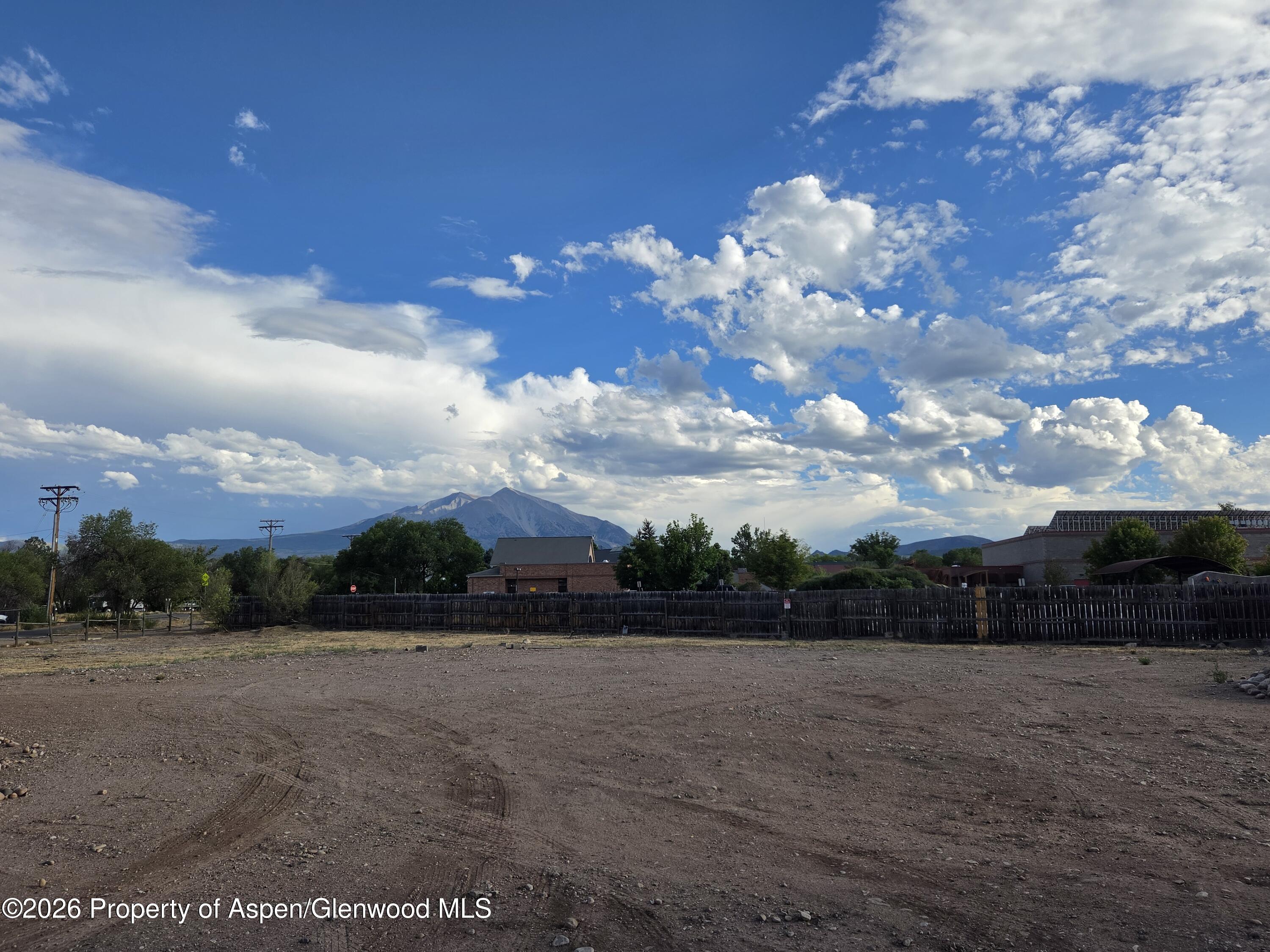 Vacant gravel storage lot with a wooden fence and mountain views beyond.